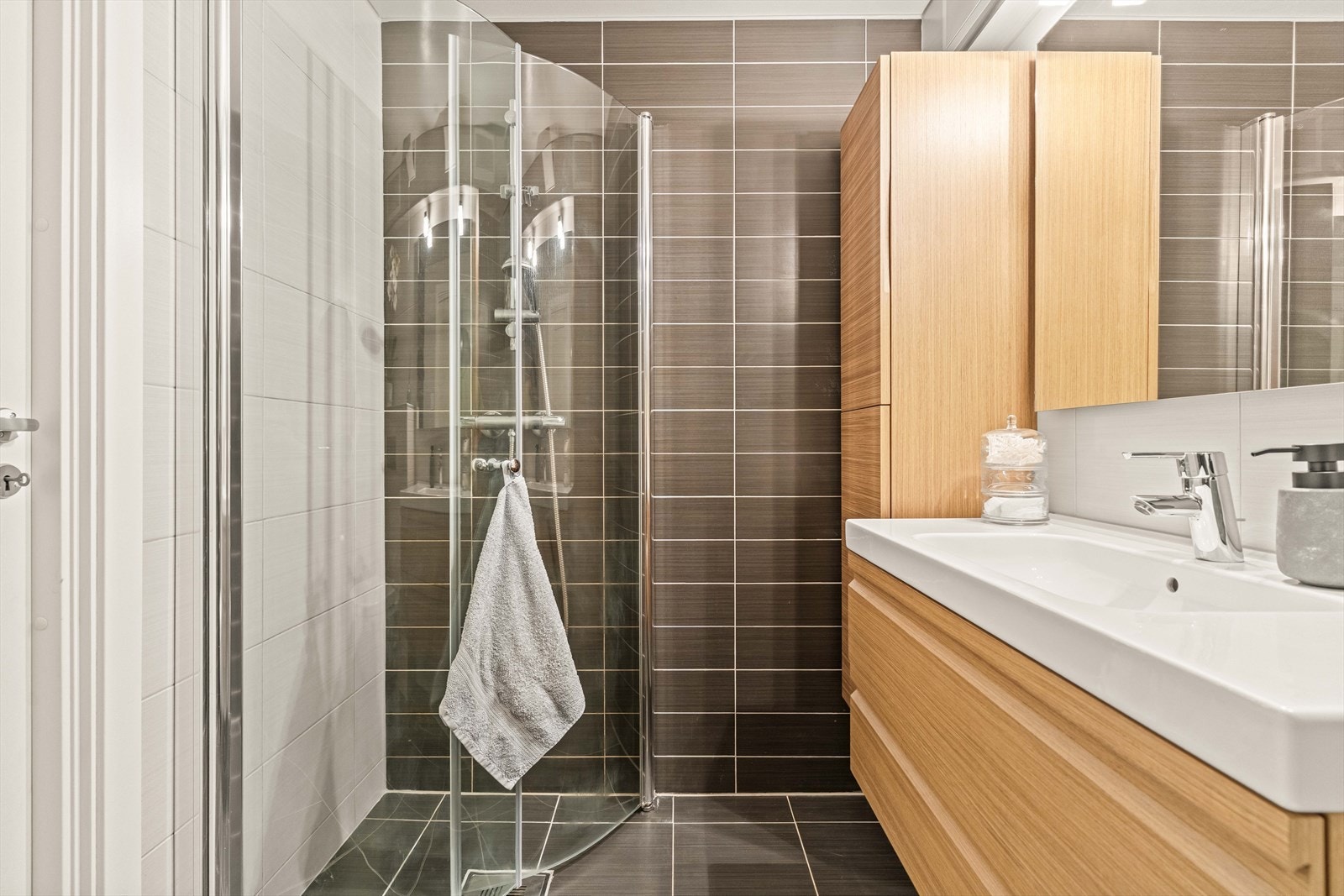 Badet er innredet med innredning med glatte fronter og porselenvask med 1 greps servantbatteri, overskap med speilfronter og lys, dusj på gulv med dusjvegger i glass, og vegghengt klosset med innebygget sisterne. Galleribilde