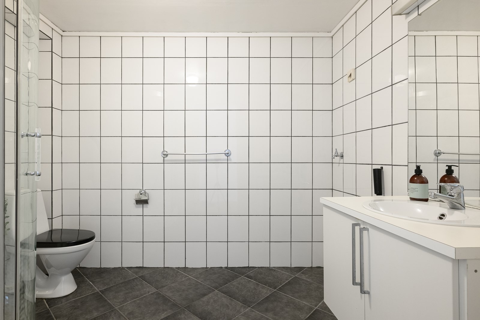 Badet i utleiedelen har fliser på gulv og vegger, gulvvarme og opplegg for vaskemaskin. Galleribilde