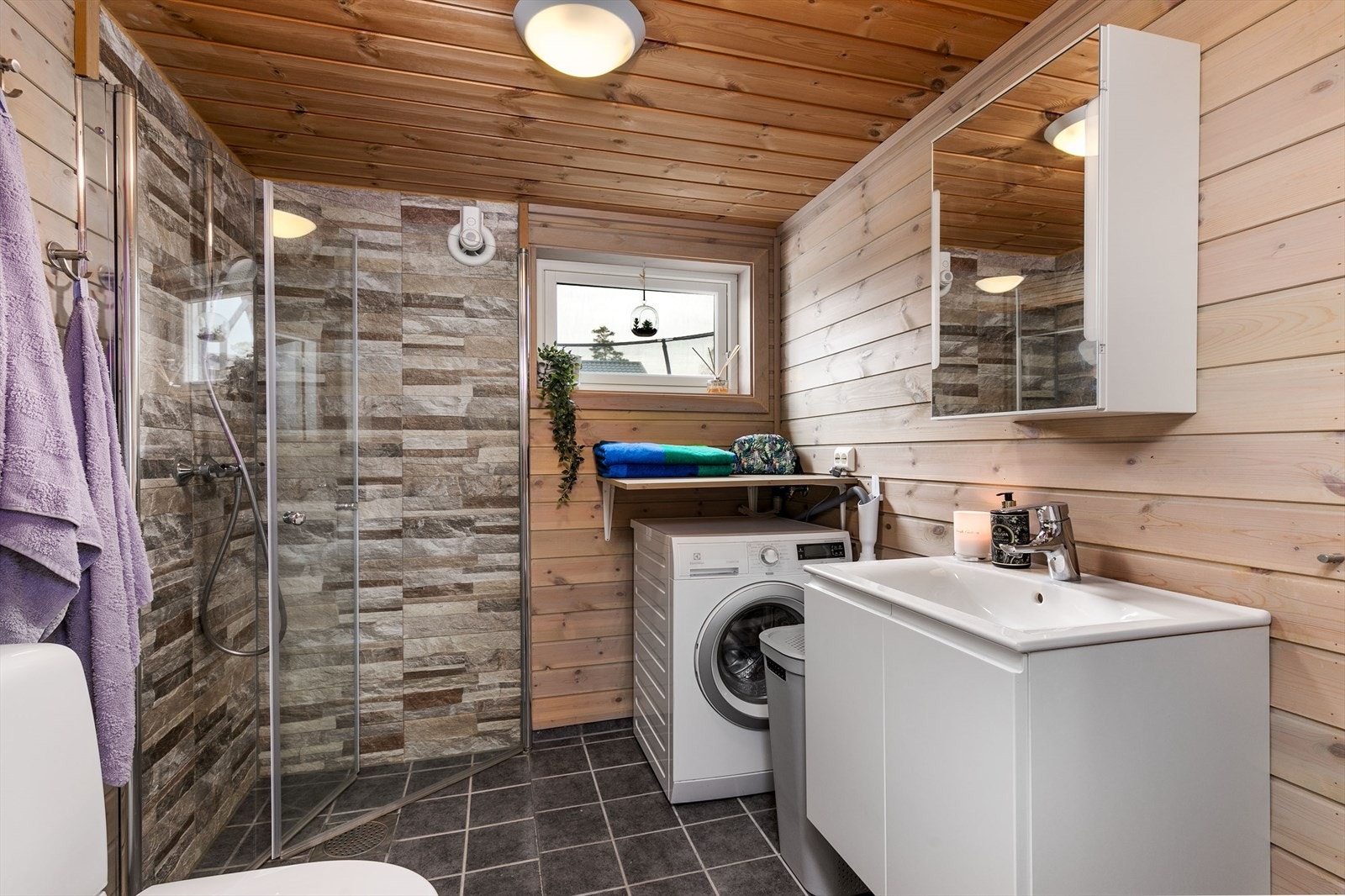 Badet fremstår som velholdt og delikat, med lasert panel på veggene, dekorstein i dusjsonen og koksgrå fliser på gulv med gulvvarme. Galleribilde