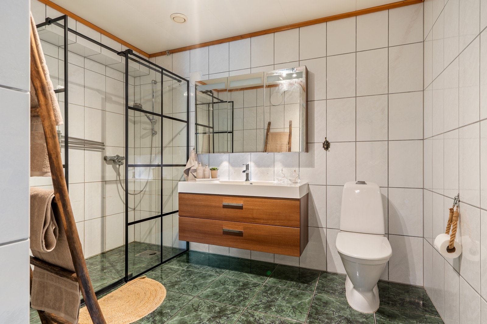 Badet er helfliset og inneholder servant i møblement, speilsskap, toalett og dusjhjørne. Galleribilde