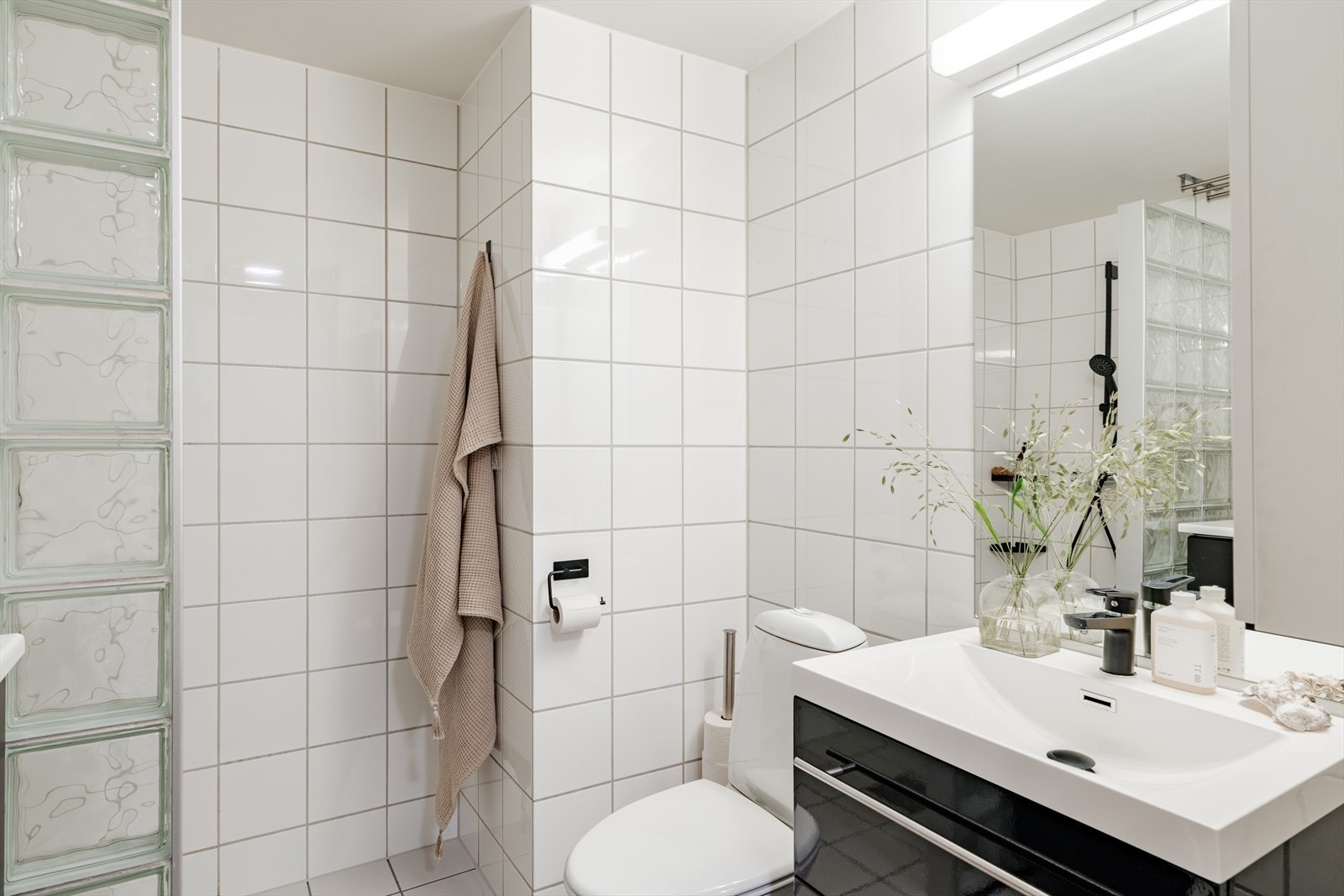 Badet er innredet med gulvstående toalett, baderomsinnredning med speil samt. dusjnisje. Galleribilde