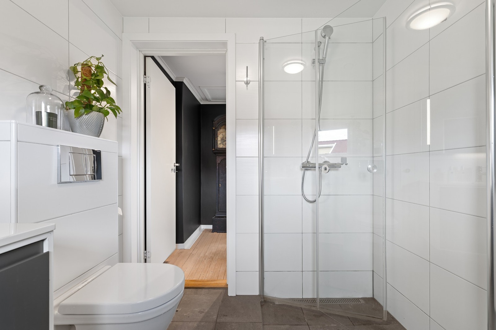 Et dusjhjørne har plassbesparende vegghengte glassdører. Badet har varmekabler i gulv Galleribilde