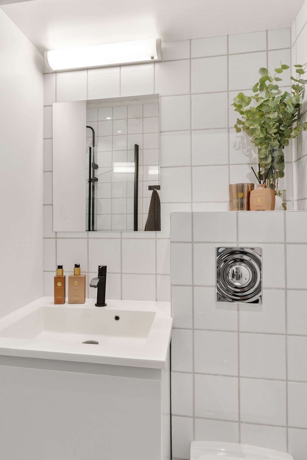 Badet er utstyrt med vegghengt toalett og dusjhjørne med glassdører og baderomsinnredning med servant og speil. Galleribilde