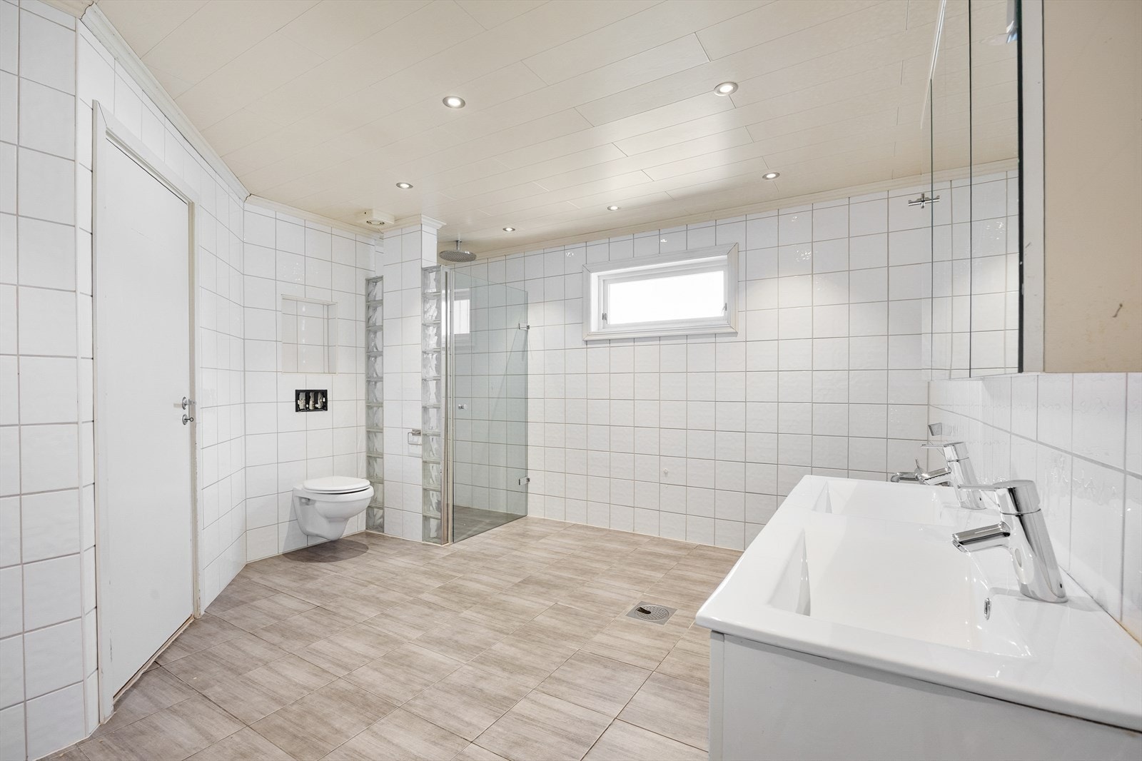 Badet er utstyrt med veggmontert toalett, dusjhjørne og en bred servantinnredning med to servanter. Galleribilde