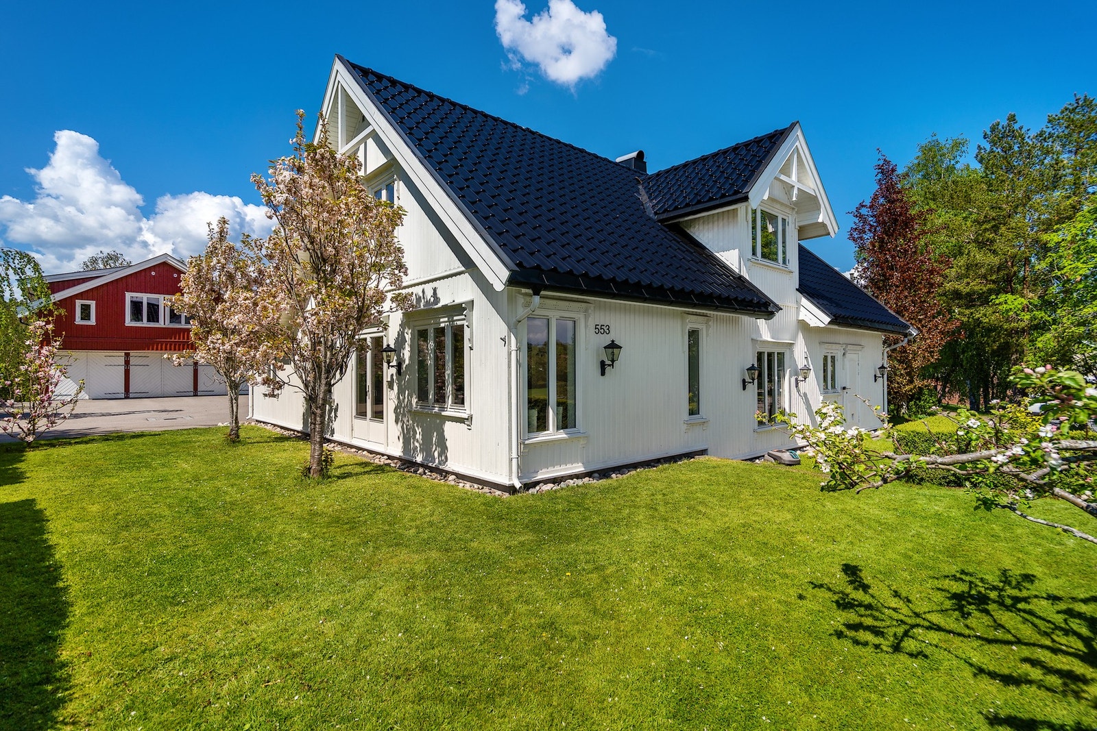 Stilren og innbydende enebolig med flott opparbeidet tomt og gjennomført uteområde. Boligen fremstår svært velholdt med moderne uttrykk, lys fasade og pent anlagt hage med grønne plenarealer, prydbusker og vakre blomstrende trær. Galleribilde