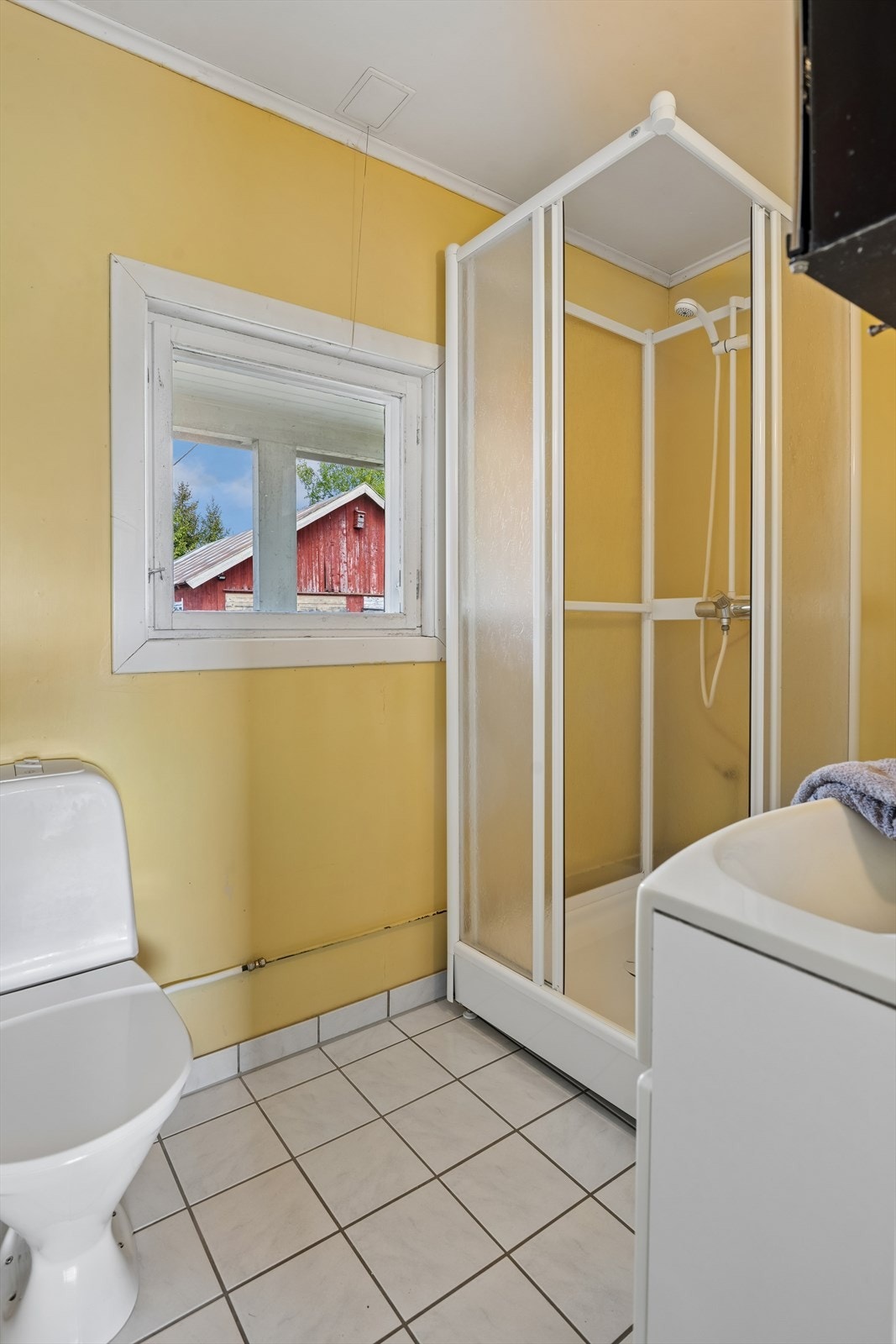 Badet er innredet med flislagt gulv, dusjkabinett og lyse overflater. Rommet har behov for oppgradering på sikt iht. tilstandsrapport. Galleribilde