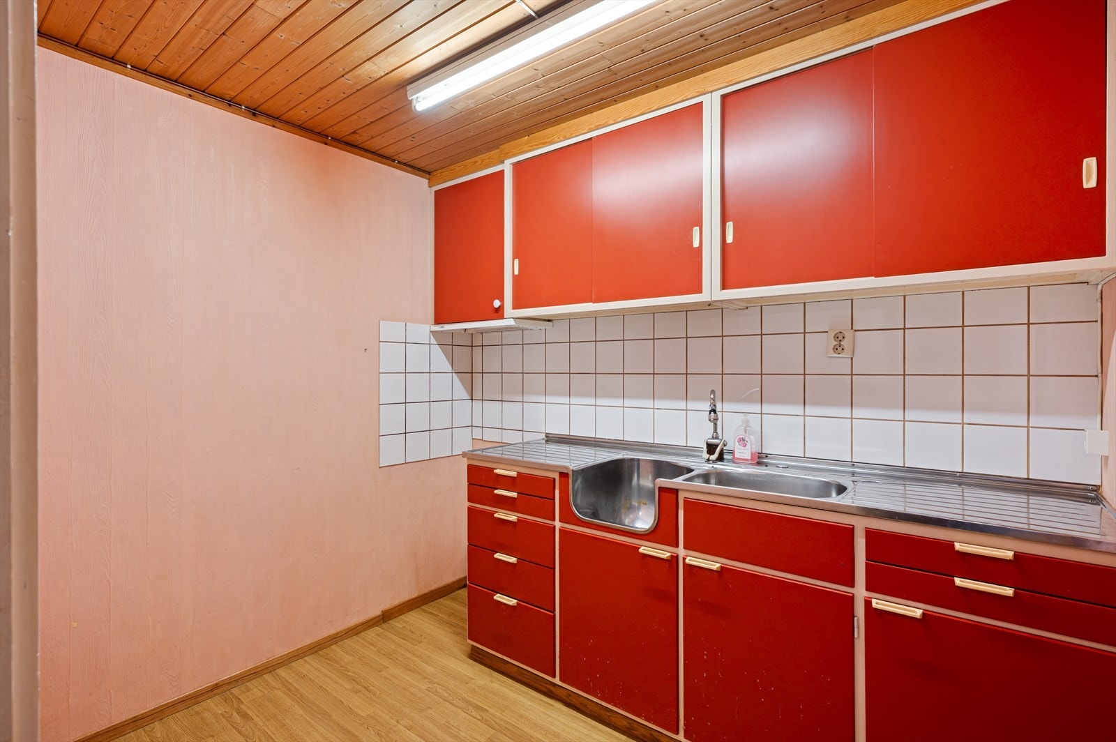 I underetasjen har kjøkkenet eldre innredning med benkeplate i stål og slette fronter. Det er opplegg for komfyr, integrert kjøkkenvifte og fliser mellom benkeplate og overskap. Galleribilde
