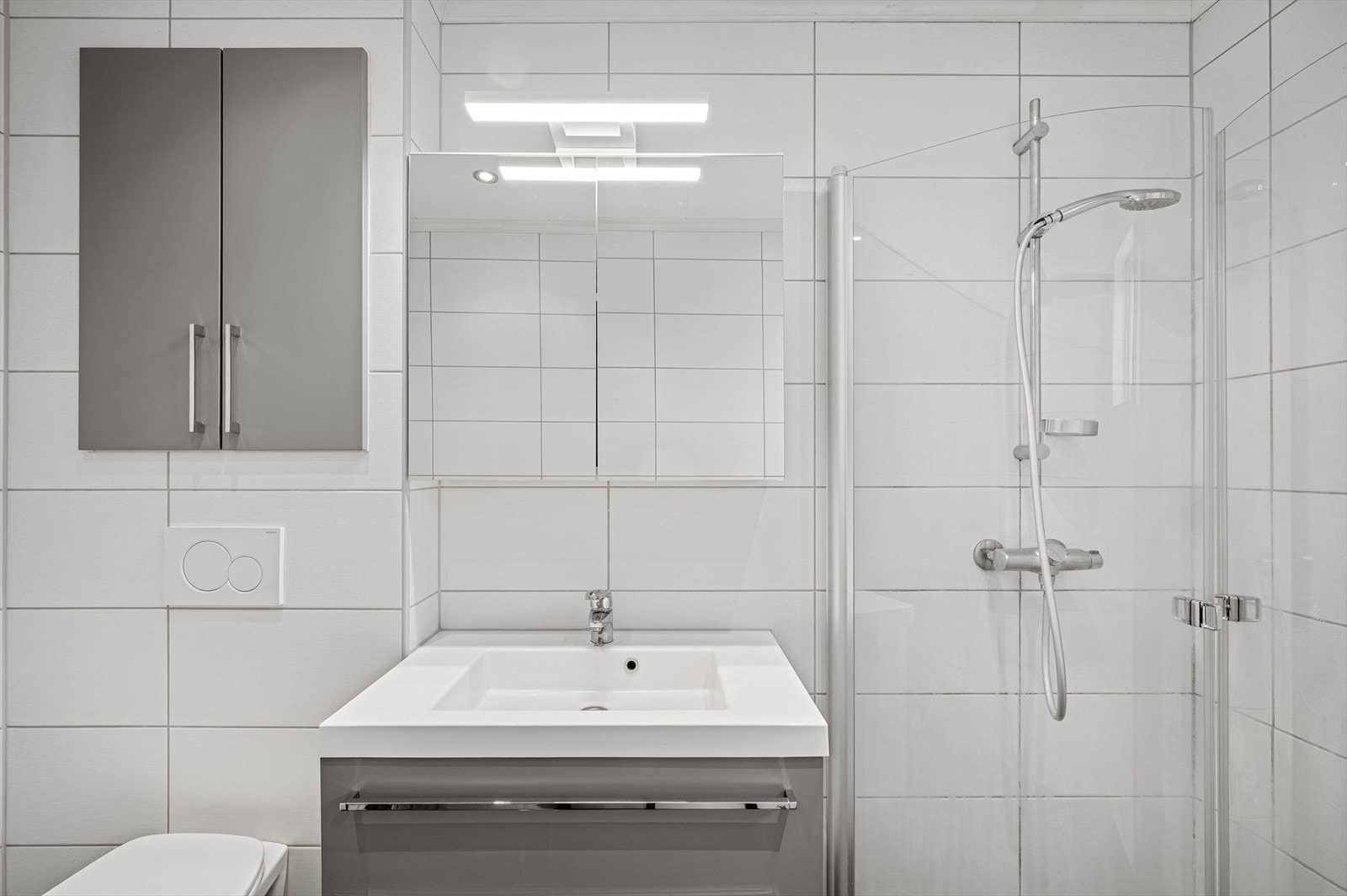 Det er fall til sluk, plastsluk og smøremembran. Badet er innredet med vegghengt toalett, dusjhjørne m/glassdører, veggskap og servant med innredning/speilskap/belysning. Galleribilde