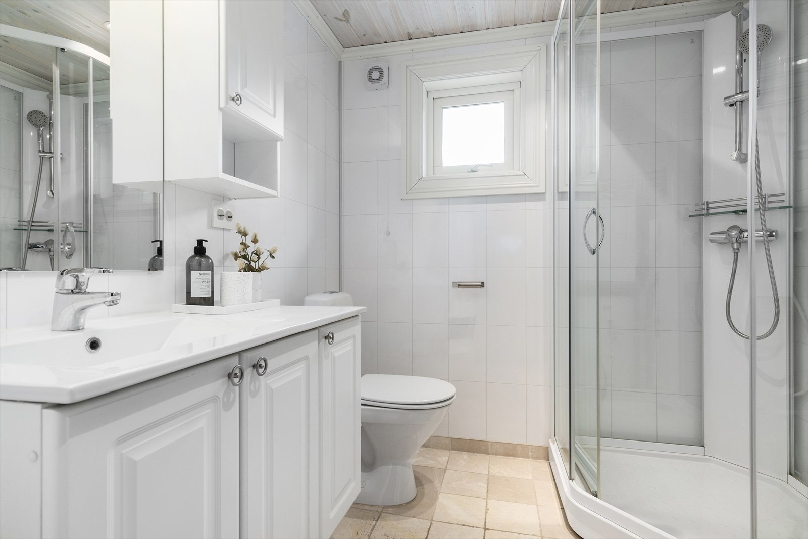 Badet har fliser på gulvet og våtromsplater på veggene. Her er dusjkabinett, toalett og innredning med servant. Galleribilde