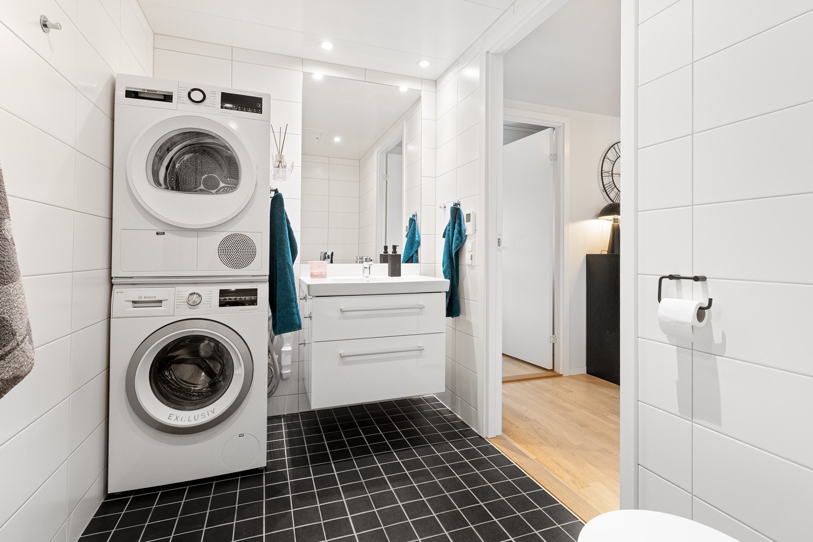 Badet er innredet med servant i baderomsinnredning, speil vegghengt toalett, dusjhjørne og opplegg for vaskemaskin. Galleribilde