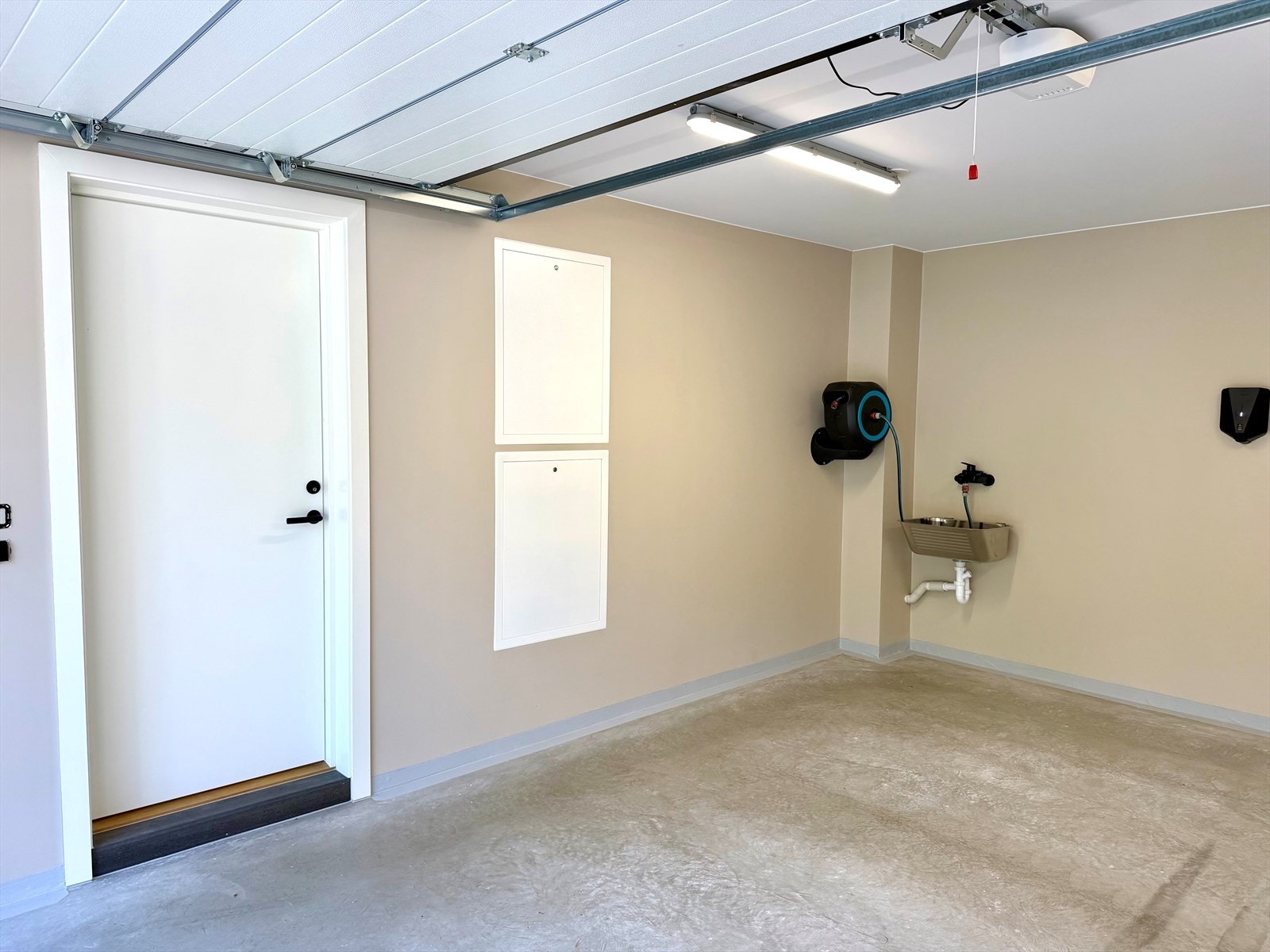 Romslig garasje for en bil med elektrisk styrt portåpner samt dør direkte inn i boligen. Garasjen har også elbil-lader, utslagsvask og vann lagt opp bakerst. Galleribilde