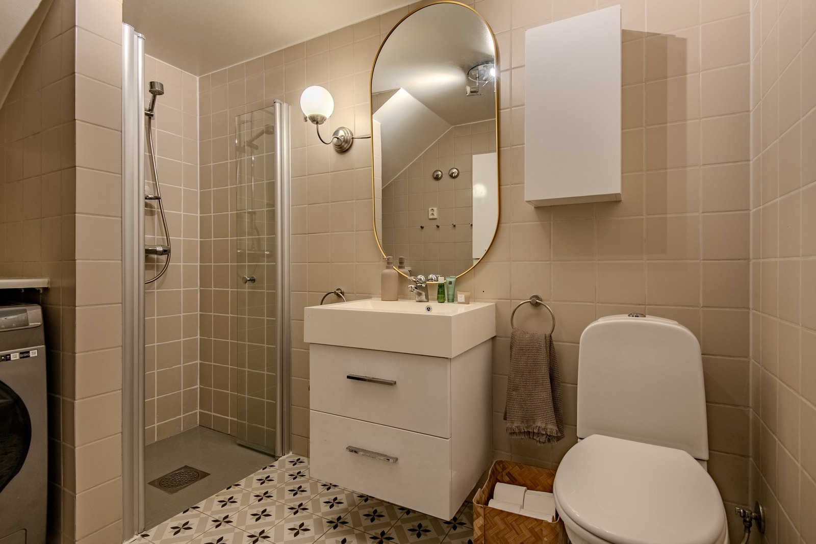 Praktisk og funksjonelt bad med flislagte vegger, dekorativt mønstergulv og varmekabler. Badet er innredet med skuffeinnredning, servant og dusjhjørne, og har opplegg for vaskemaskin - alt samlet i én god løsning. Galleribilde