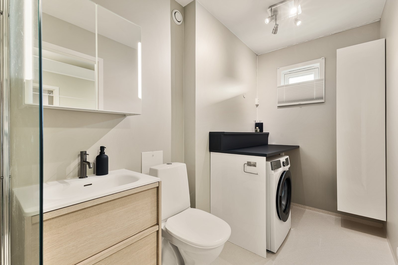 Badet er innredet med møblement/speil, belysning, toalett, dusjgarnityr og dusjhjørne samt praktisk opplegg for vaskemaskin i rommet. Galleribilde