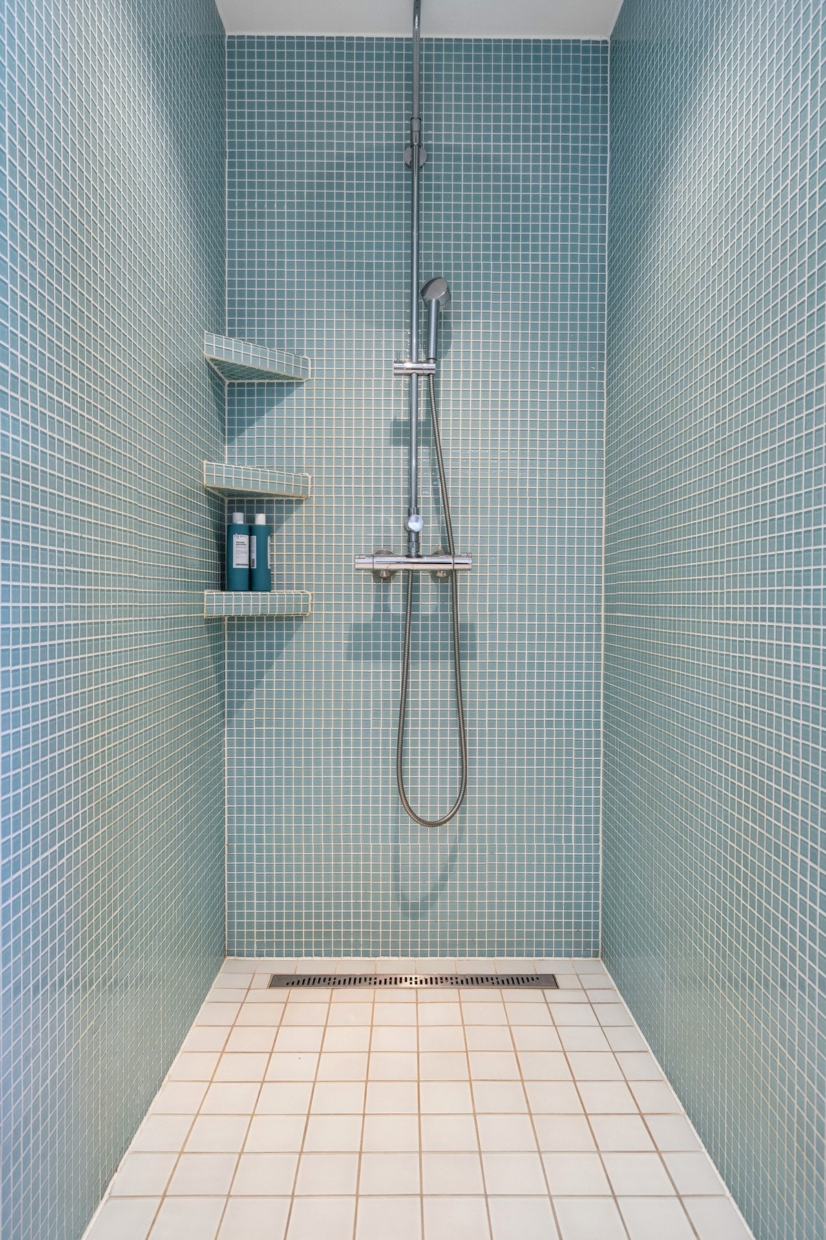Dusjsonen i hovedbadet er flislagt med mosaikkfliser og har integrerte hyller for oppbevaring. Galleribilde