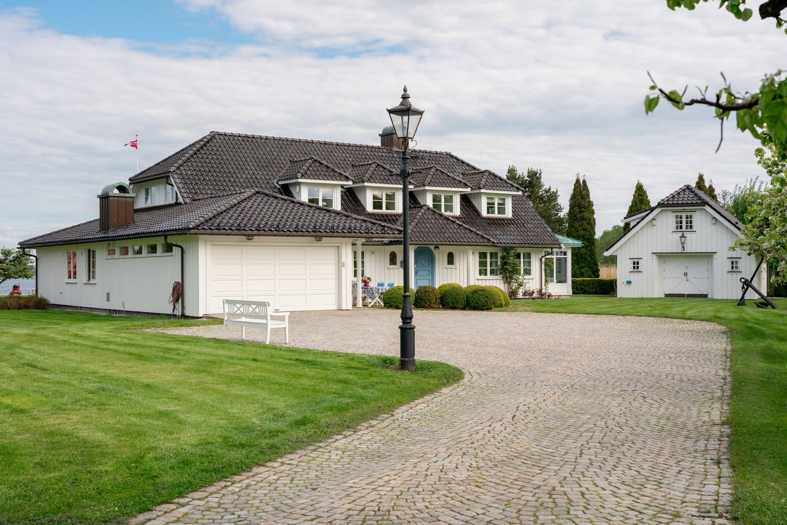 Stor og representativ gårdsplass med brosteinsbelagt adkomst, dobbelgarasje og frittstående uthus. Galleribilde