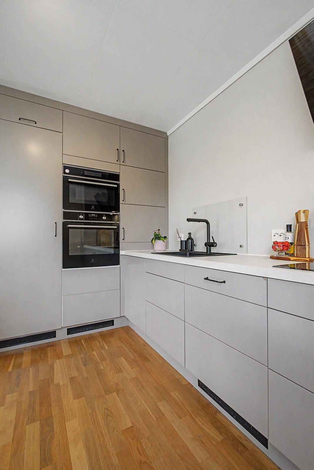 Innredning fra Epoq med malte skapfronter og takhøye skap | laminat benkeplater med nedfelt vask og platetopp | glassplater på vegg ved vasken og platetoppen | Integrert kombi/mikroovn, stekeovn, oppvaskmaskin og kjøleskap Galleribilde