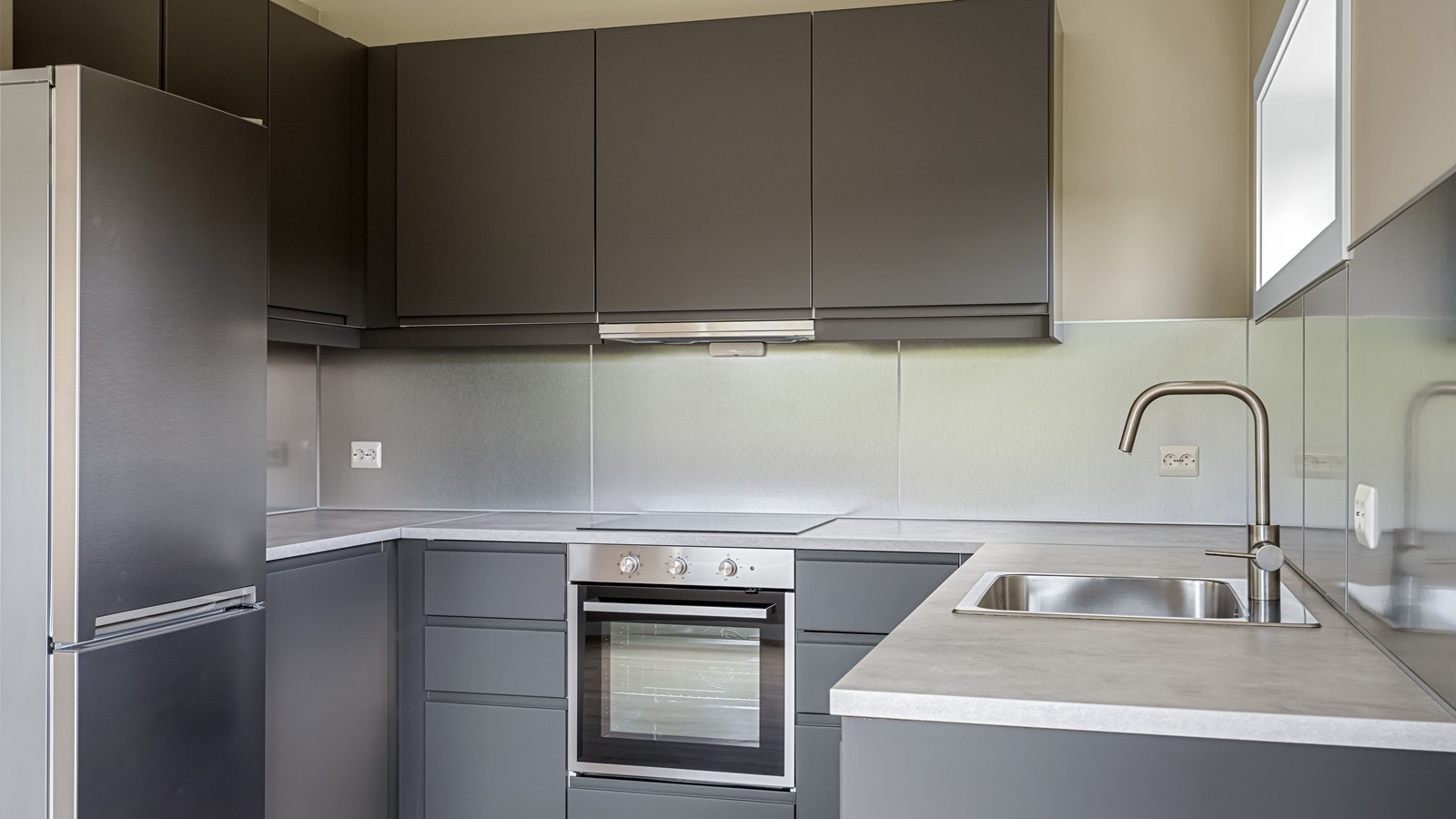 Lekkert kjøkken utstyrt med integrert platetopp, stekeovn og oppvaskmaskin, og frittstående kjøl/fryseskap. Galleribilde