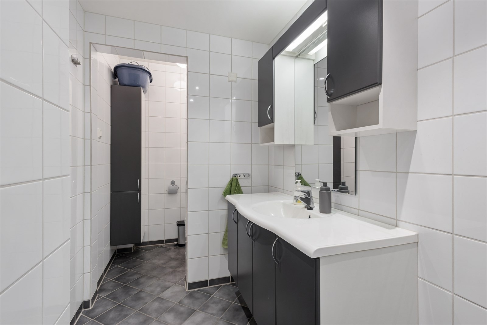Badet har innredning med nedfelt servant, veggmontert toalett, dusjhjørne og opplegg for vaskemaskin. Galleribilde