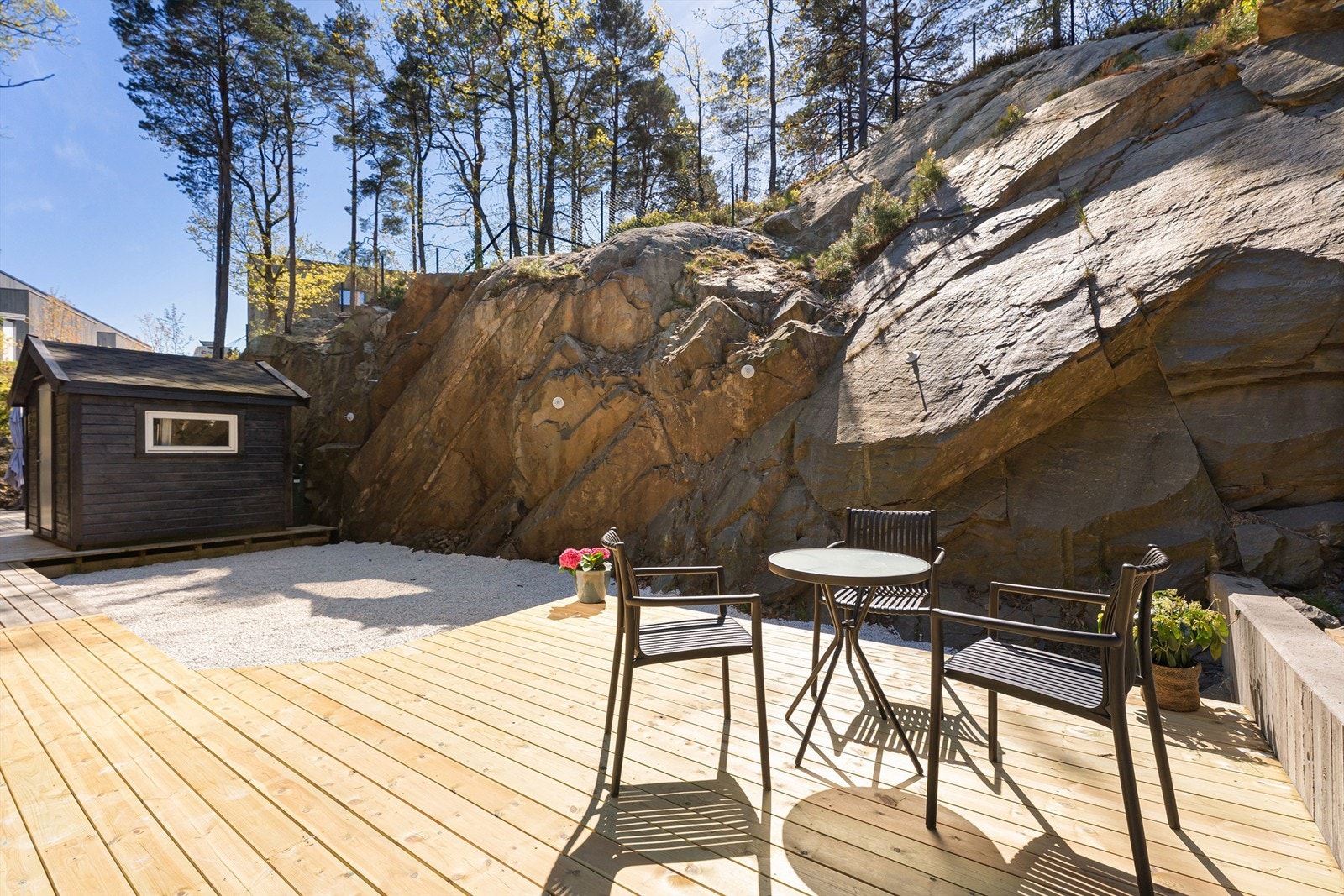 Uteområde på bakside som går i ett med naturen med terrasse og lyse stein som gir en kontrast til den moderne kledningen til huset Galleribilde