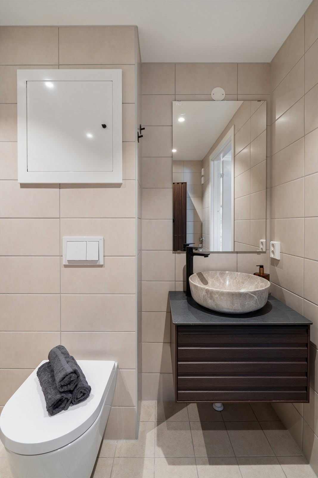Badet er innredet med dusjhjørne med skjermvegg av glass, vegghengt toalett med innebygget sisterne, servantskap med bolleservant, ett-greps blandebatteri, to høyskap og speil. Galleribilde