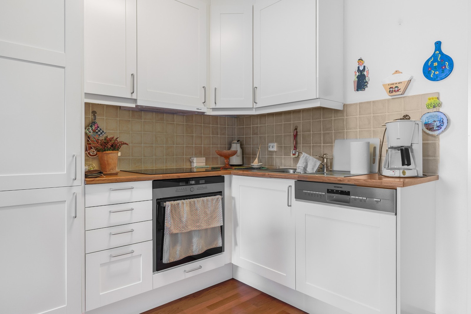 Bildet viser leilighetens kjøkken. Kjøkkenet er utstyrt med integrerte hvitevarer som stekeovn, kjøl-/frys og oppvaskmaskin. Over kokesonen henger ventilator tilkoblet sentralt ventilasjonssystem. Galleribilde