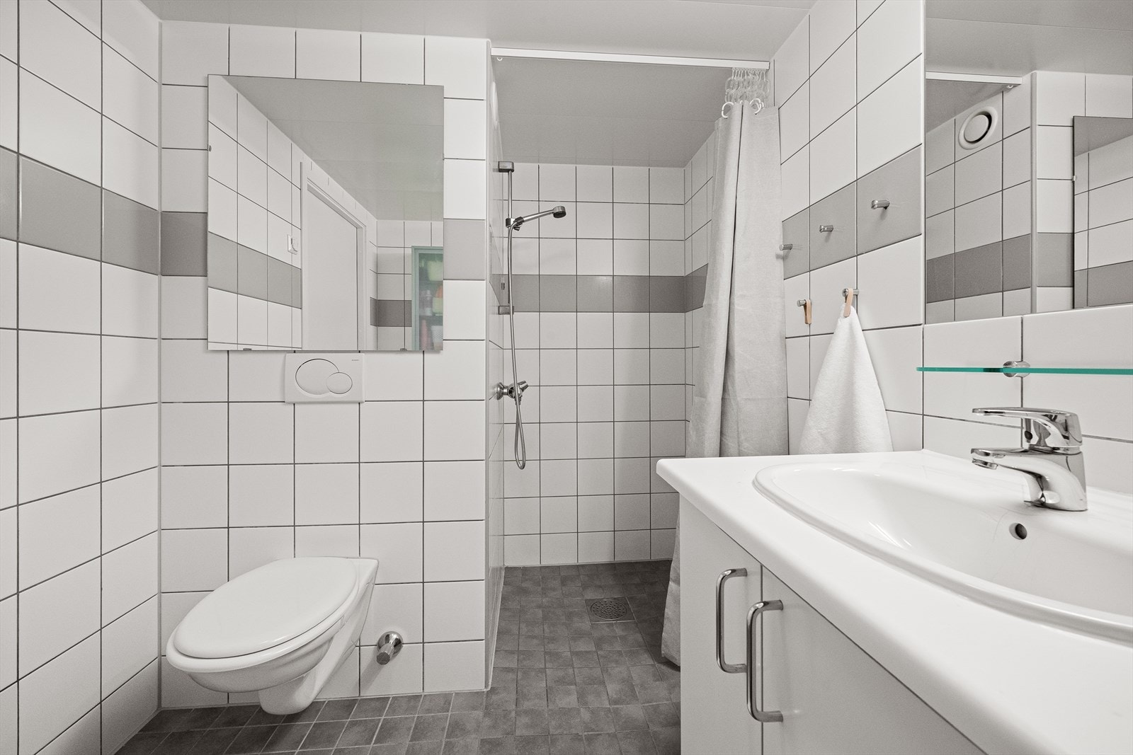 Badet er helfliset og utstyrt med vegghengt toalett, servant med underskap og dusjhjørne. Galleribilde