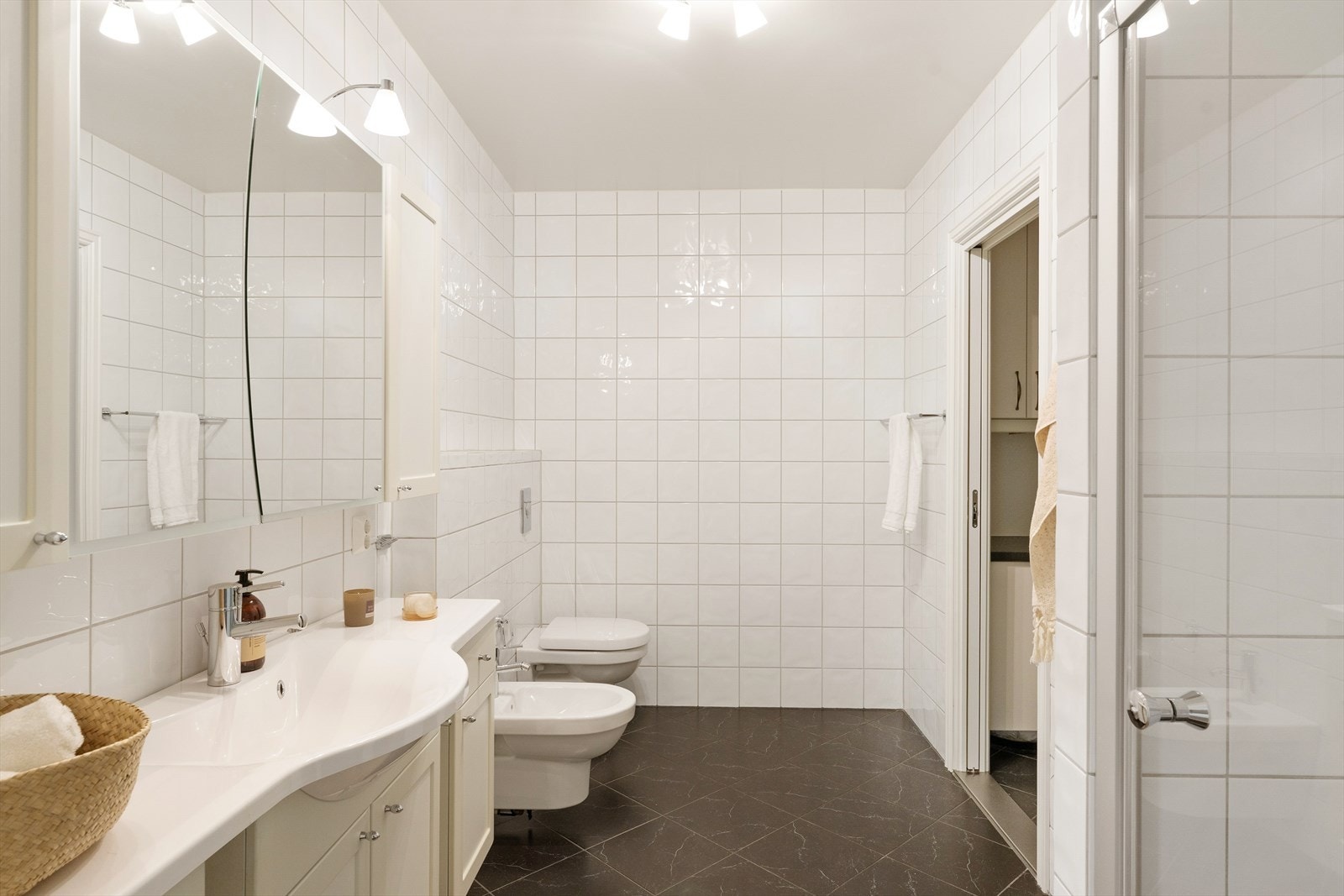 Badet er utstyrt med veggmontert toalett, bidé, dusjnisje og servant i baderomsinnredning. Galleribilde