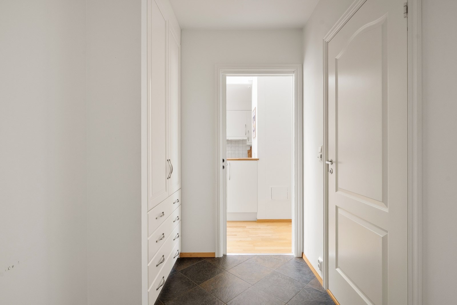 Fra utvendig overbygget trappeoppgang (der det også er heis), har man egen inngang inn til entréen. Gulvet er flislagt, og langs veggen til venstre er det innredning med skap og skuffer som gir god plass til yttertøy og sko. Galleribilde
