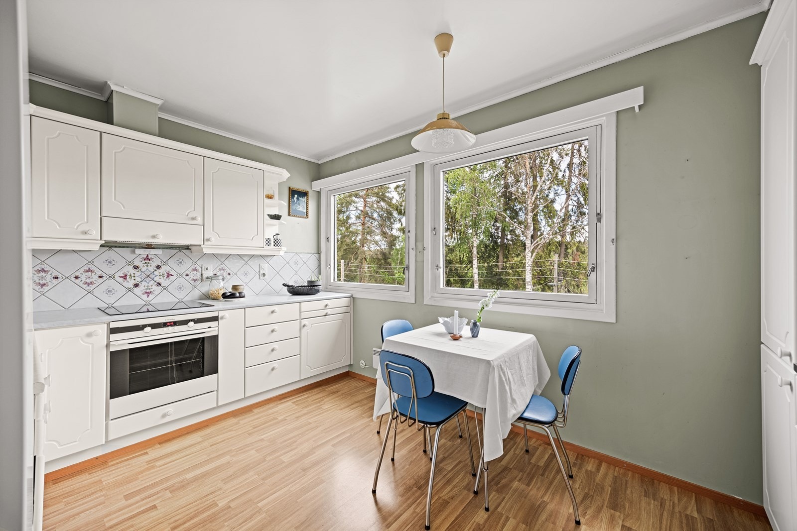 Romslig kjøkken i separat rom med eldre kjøkkeninnredning med profilerte, folierte fronter og enkelte vitrinefronter. Kjøkkenet er utstyrt med laminatbenkeplate med heldekkende kum i rustfritt stål, fliser over benkeplate og belysning under overskap. Galleribilde