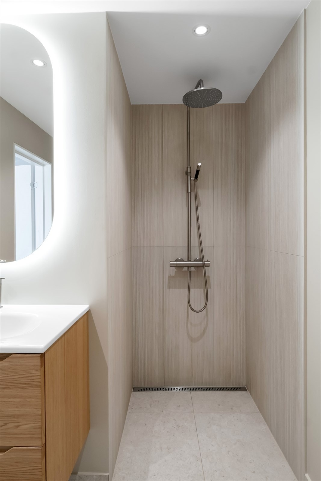 Badet er innredet med vegghengt toalett, servant med innredning med malte fronter, speil med belysning, regnfallsdusj samt opplegg for vaskemaskin Galleribilde