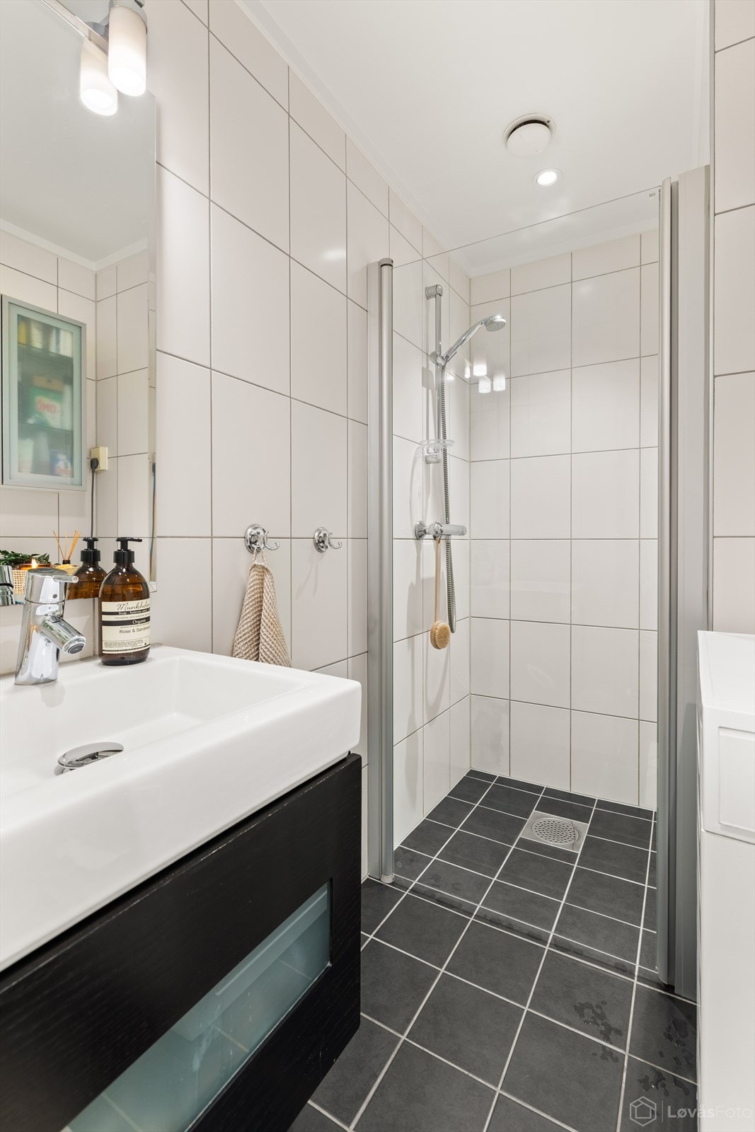 Badet er utstyrt med dusj med innfellbare glassdører, servant, vegghengt toalett samt opplegg for vaskemaskin. Galleribilde
