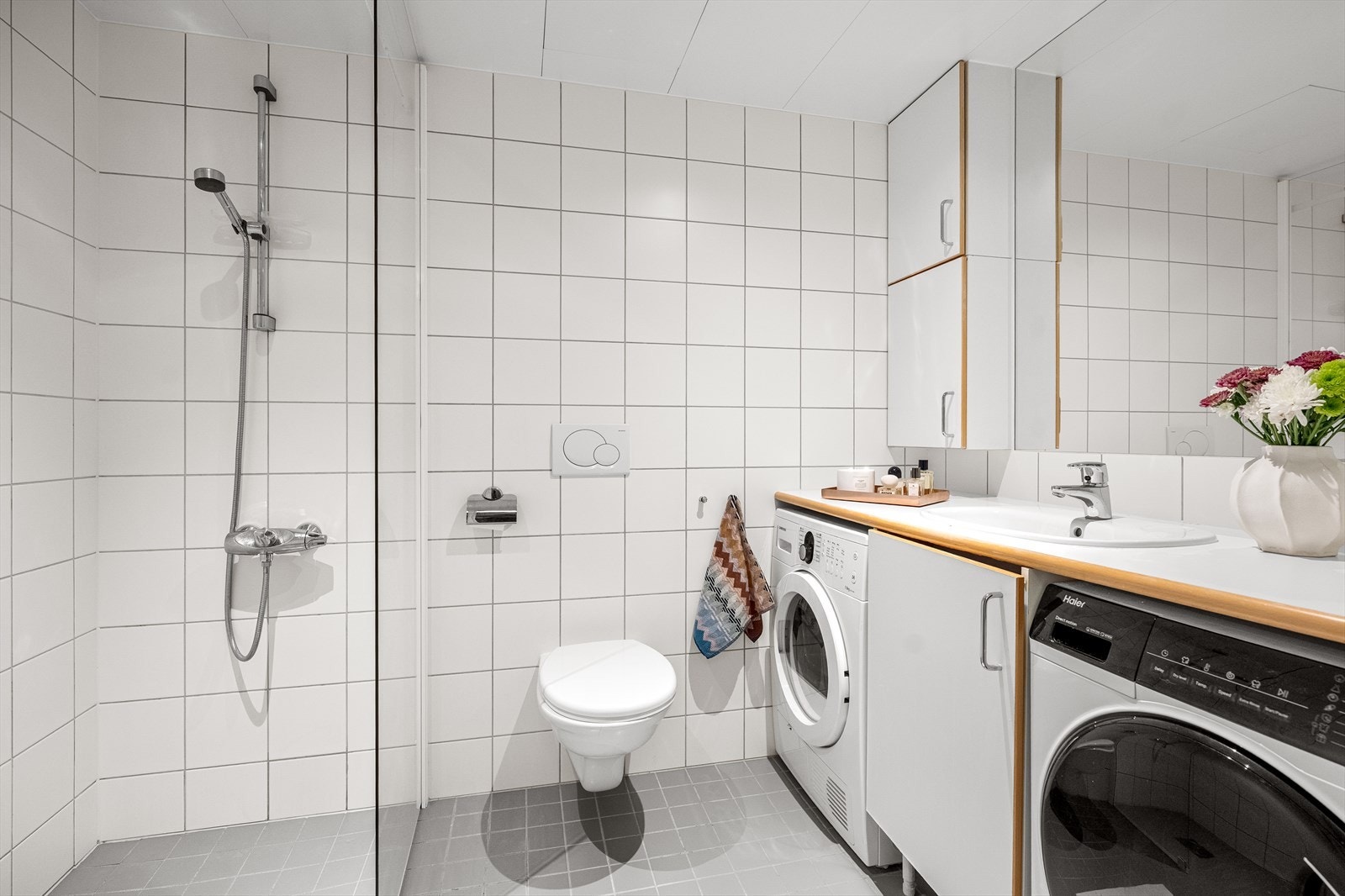 Badet er flislagt med elektriske varmekabler i gulvet. Badet er innredet med dusjhjørne, vegghengt toalett og opplegg for vaskemaskin og tørketrommel. Galleribilde