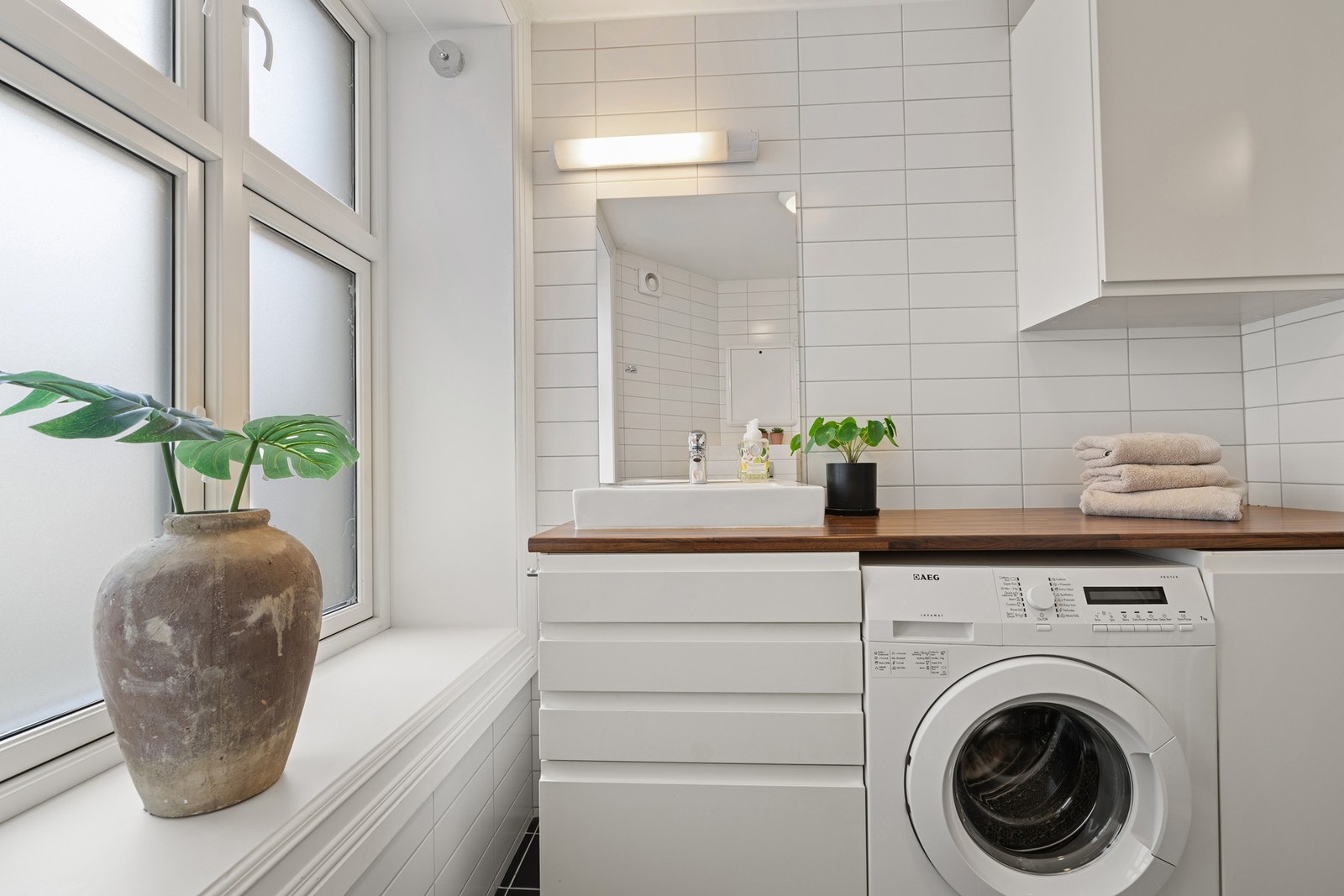 Badet er utstyrt med vegghengt toalett, servant med innredning, dusjhjørne med glassvegger og opplegg for vaskemaskin. Galleribilde