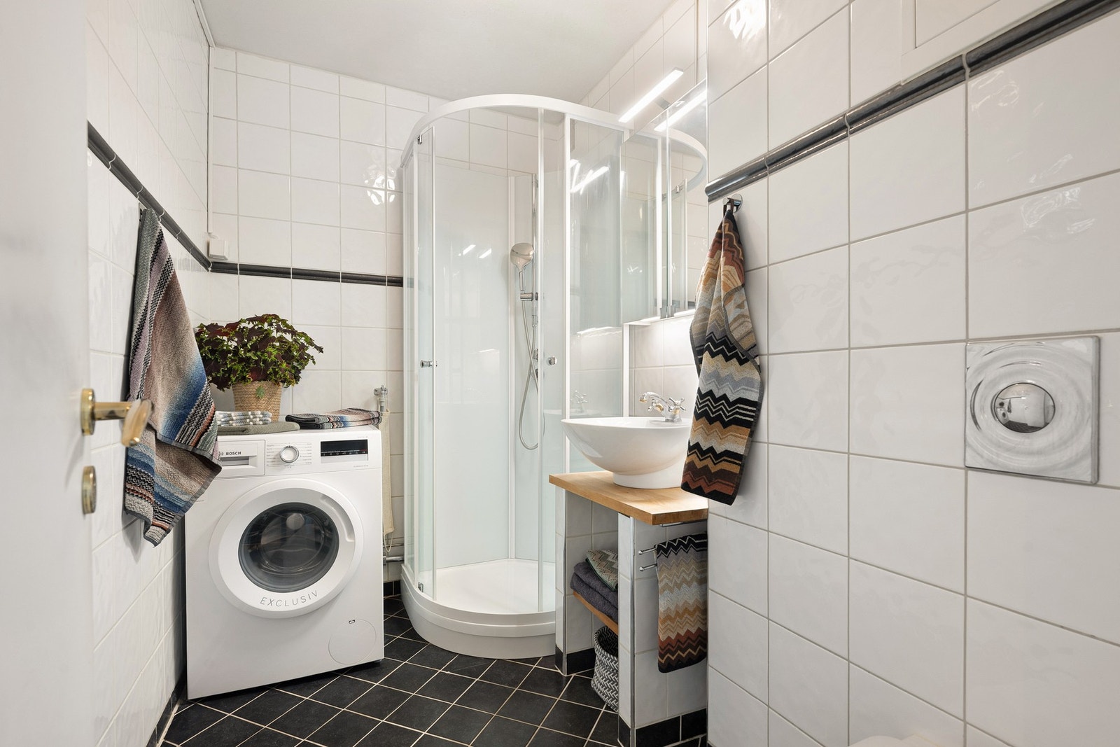 Badet er flislagt og har en praktisk innredning med servant på benk, speilskap med belysning, veggmontert toalett og dusjkabinett. Galleribilde