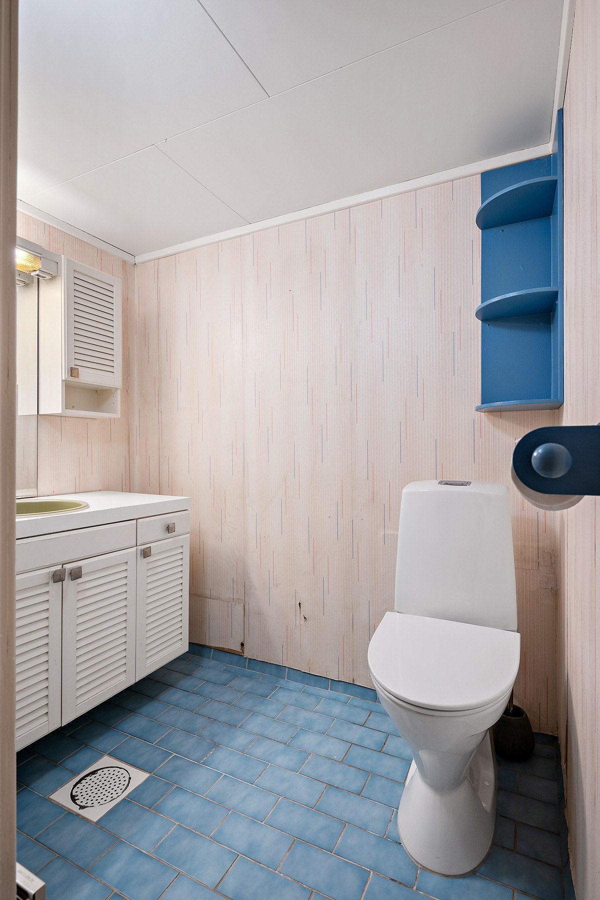 Vaskerom med flislagt gulv og tapetserte veggflater. Innredningen er bestående av servant med underskap, speil med overlys, veggskap, gulv, notert klosett og opplegg for vaskemaskin. Galleribilde