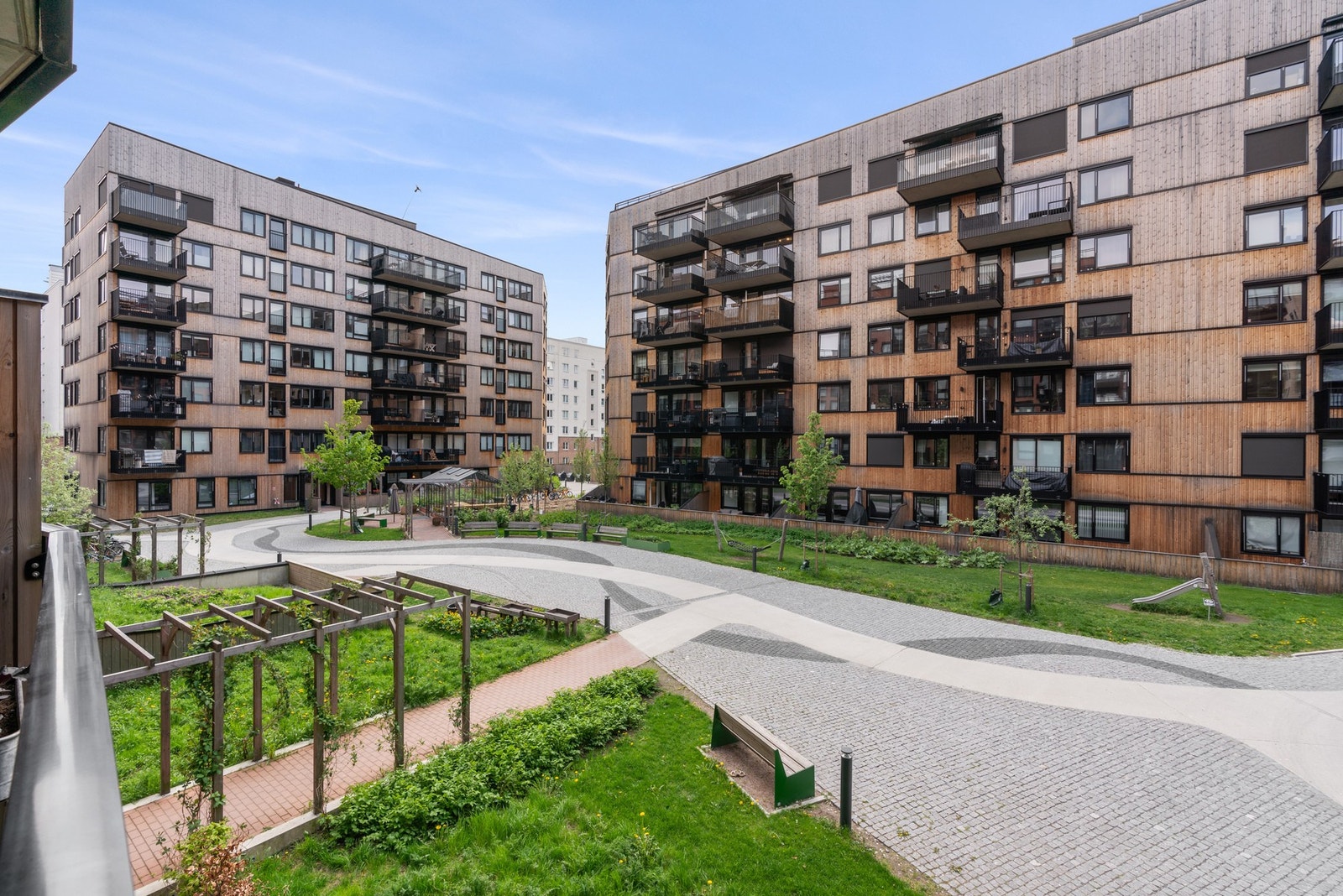 Hyggelig bakgård opparbeidet med beplantninger sittegrupper, drivhus og lekeapparater. Galleribilde