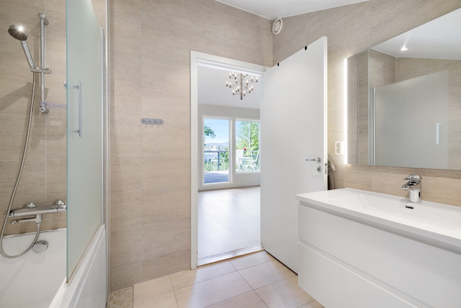 Badet er innredet med vegghengt toalett og badekar med tappekran og dusjhode. Moderne baderomsinnredning med lysspeil Galleribilde