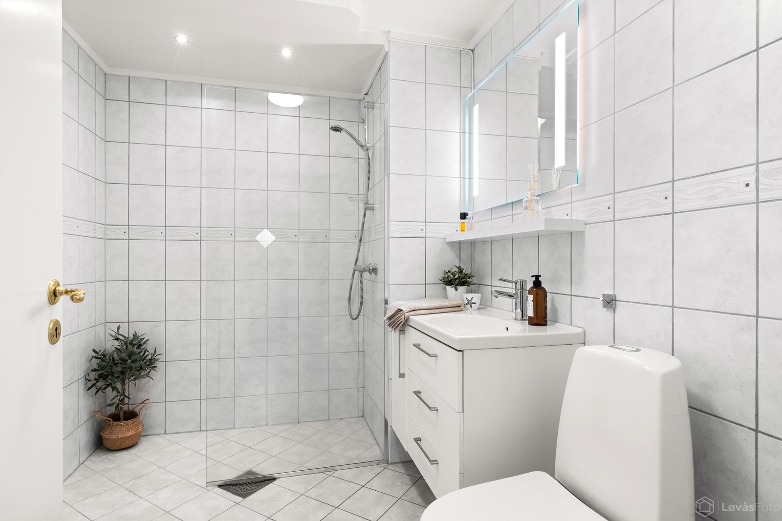 Lyst bad med varmekabler i gulv, servantinnredning, dusjløsning med glassvegg, toalett og opplegg for vaskemaskin. Galleribilde