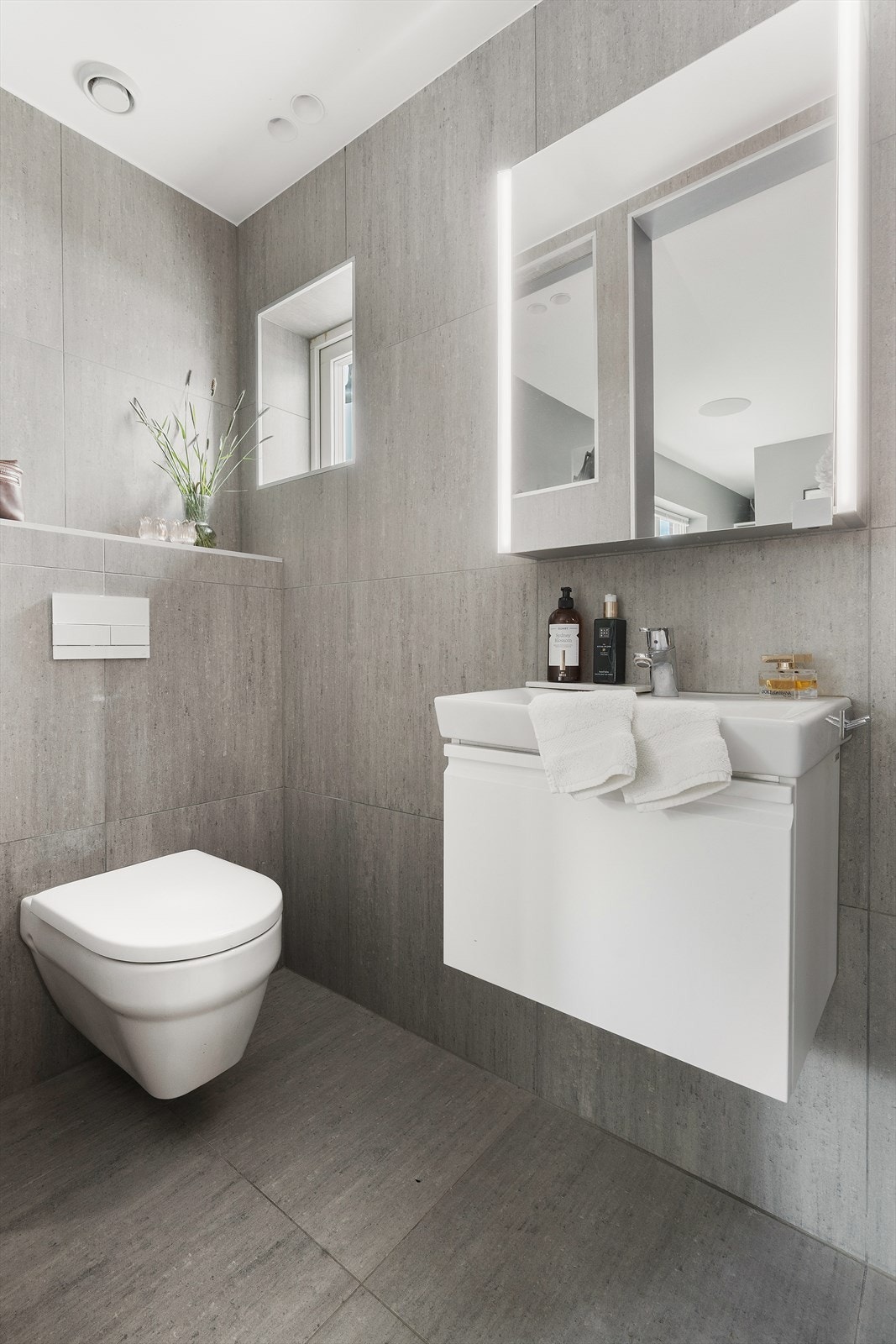 Badet er flislagt med vegghengt toalett og servant med skuffeinnredning. Galleribilde