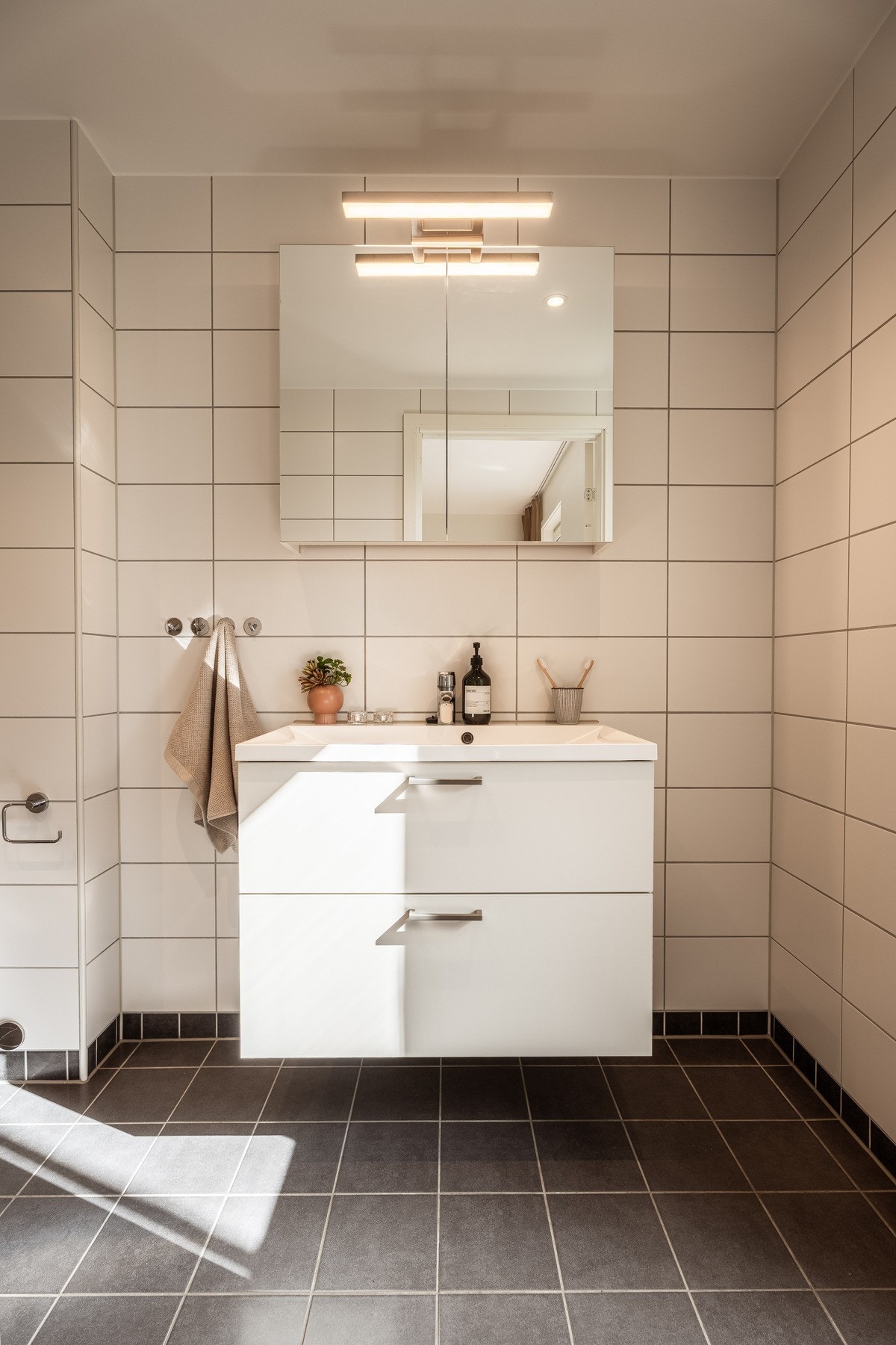 Badet har en stilren kombinasjon av helhvite vegger og mørke gulvfliser. Galleribilde