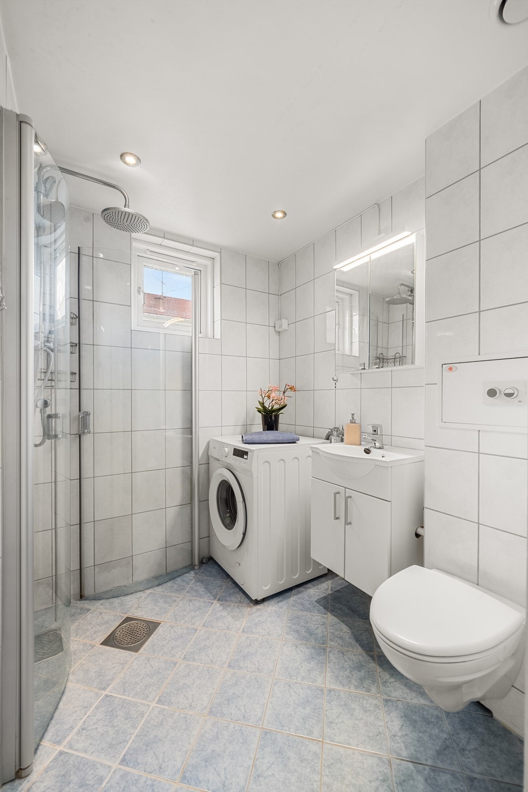 Badet er flislagt og utstyrt med vegghengt toalett, dusjhjørne og downlights i taket. Galleribilde