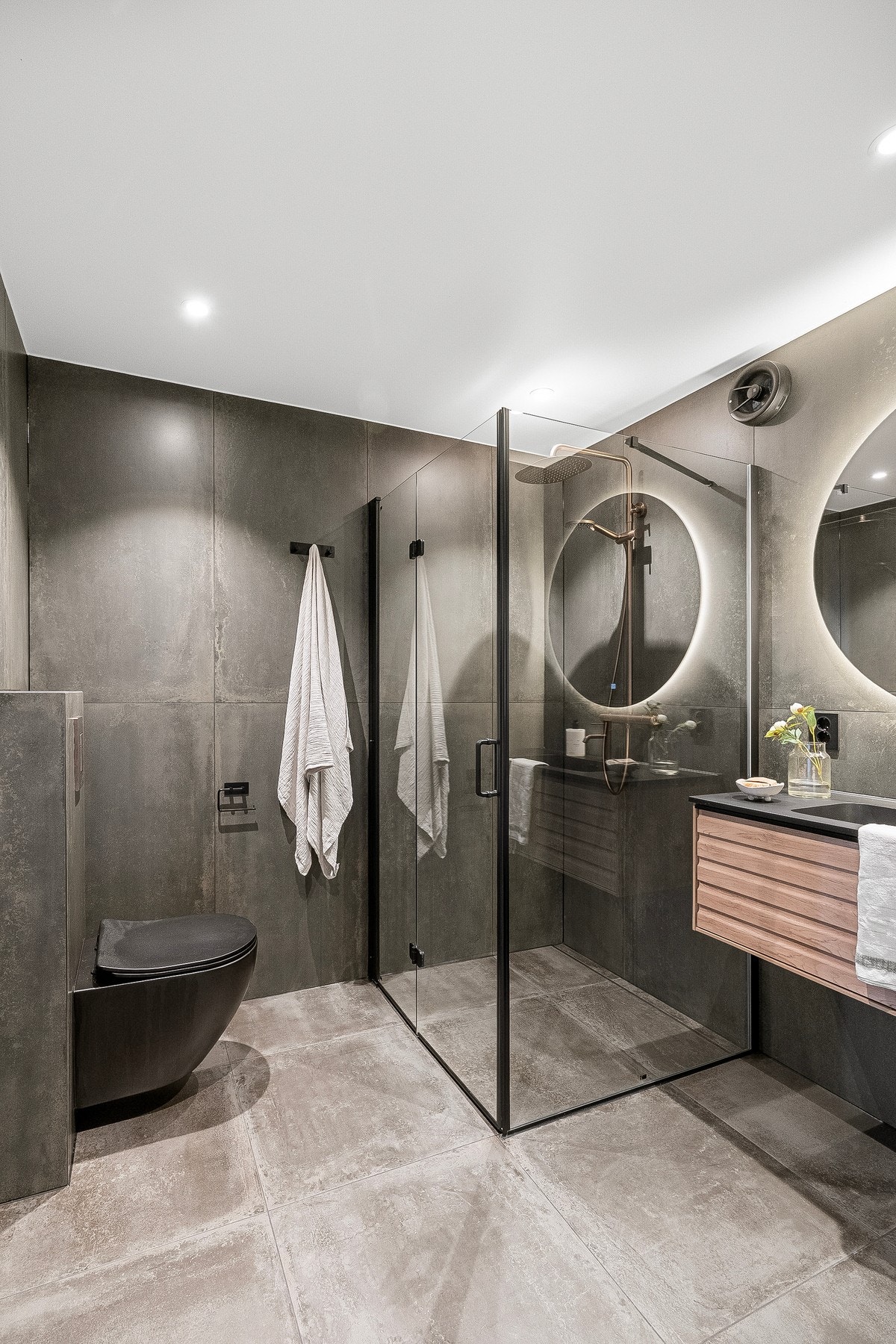 Badet fremstår stilrent med store fliser, moderne servantinnredning, vegghengt toalett og dusjløsning med glassvegger. Galleribilde