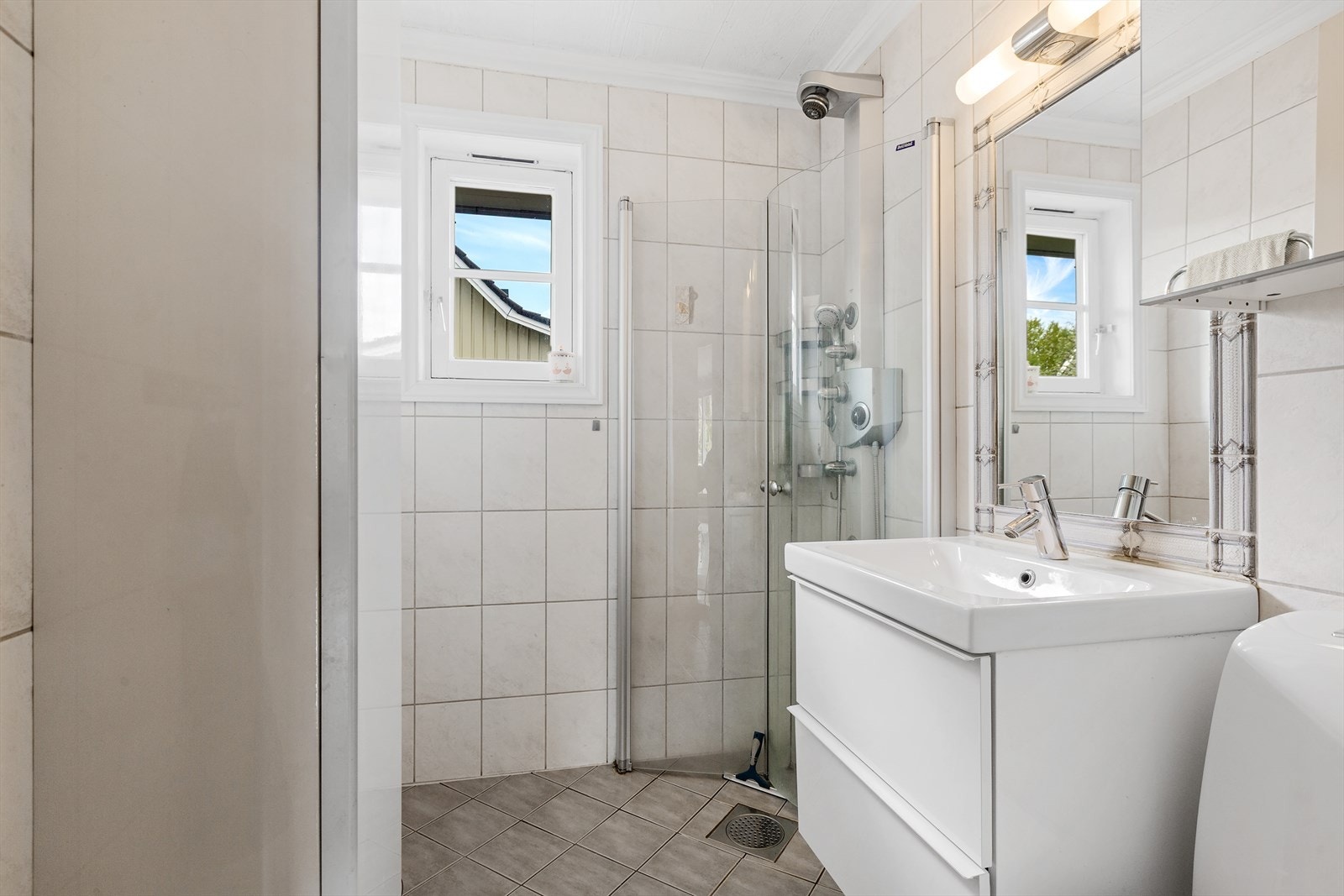 Badet har fliser på vegg og gulv- varmekabel i gulv- installert dusjhjørne- toalett- vask med underskap og speil Galleribilde