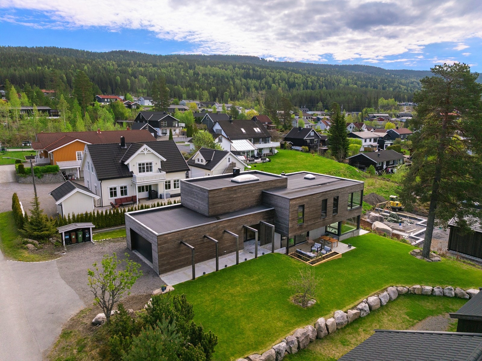 Eiendommen har et relativt flatt terreng som heller svakt ned på baksiden av boligen, noe som gir en naturlig og lun ramme rundt uteområdene. Her får du en oversiktlig og lettstelt hage med frodig plen - perfekt for både lek og avslapning Galleribilde