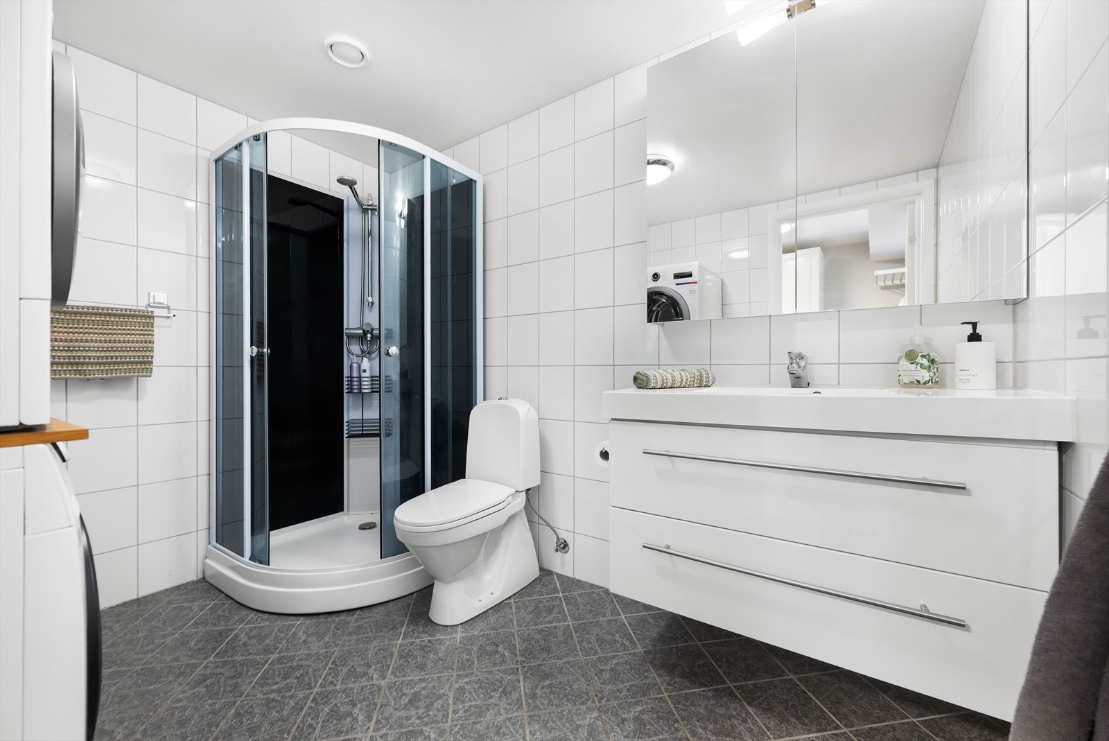 Badet er romslig og pent innredet med gulvmontert toalett, servant med benkeskap, dusjkabinett samt opplegg for vaskemaskin. Galleribilde
