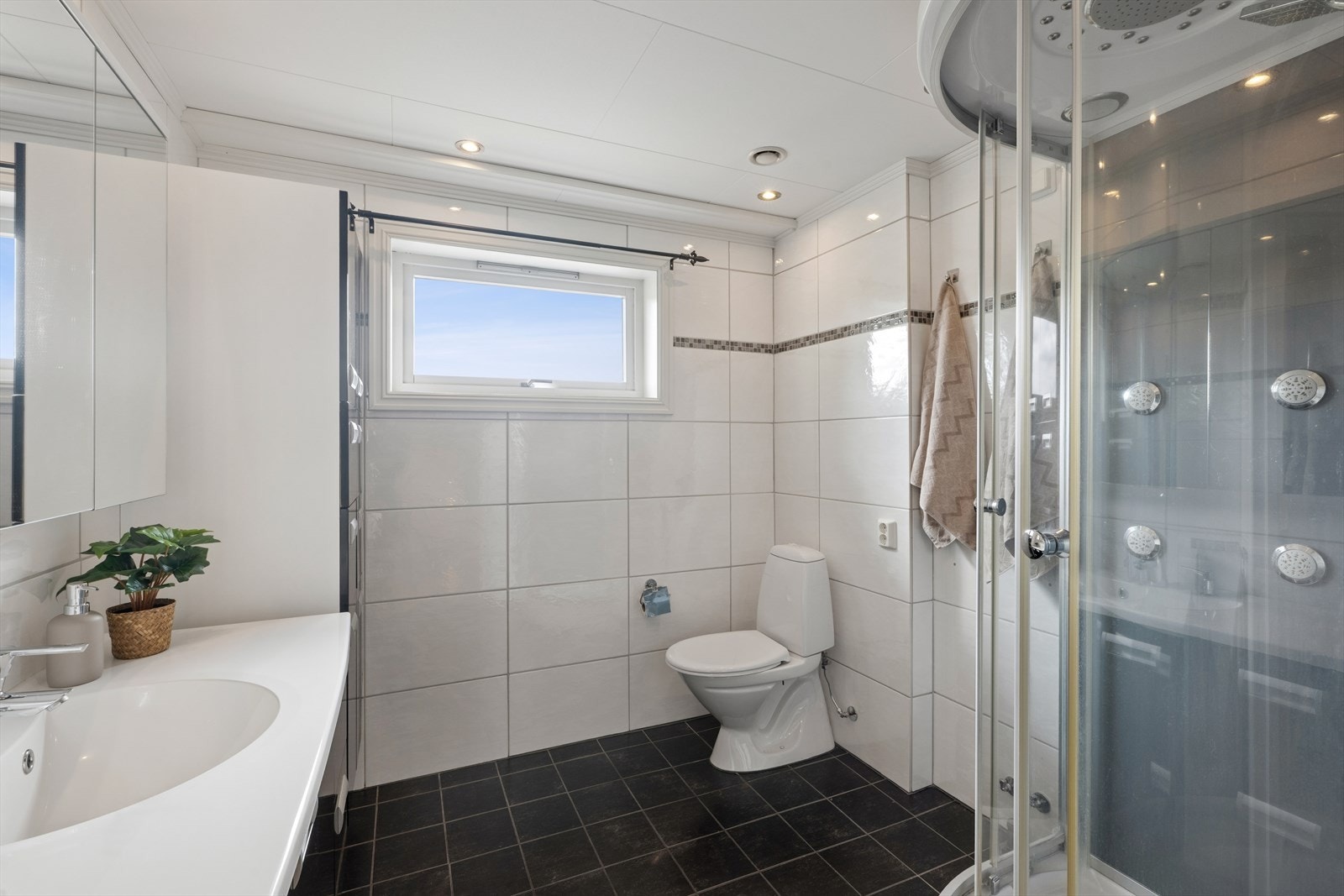 Badet i 1. etasje er romslig og pent med en kombinasjon av mørke og lyse fliser med mosaikkdetaljer. Innredningen består av klosett, servant med innredning, speilskap og dusjkabinett. Galleribilde