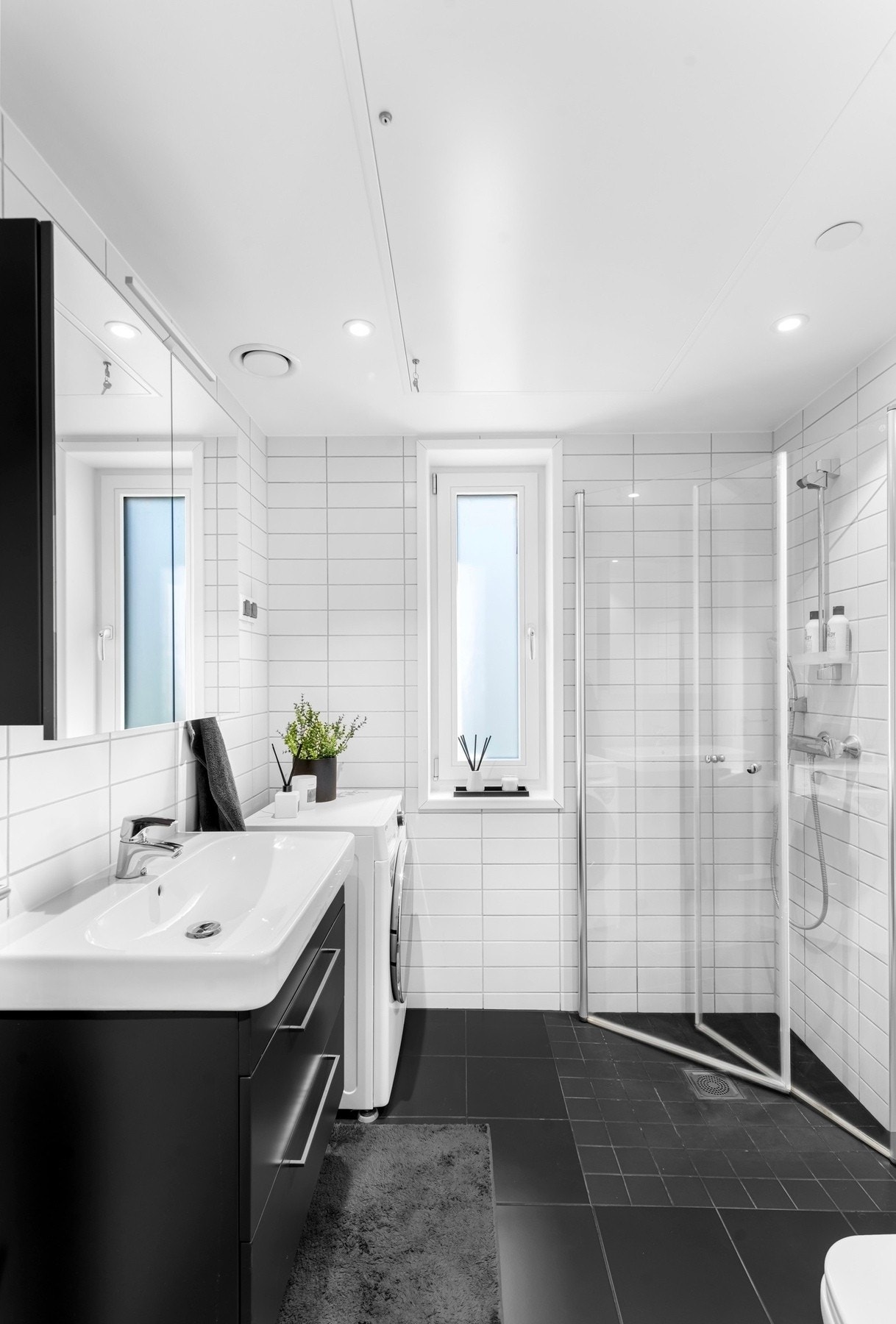 Dagene får en god start på badet, smakfullt innredet med hvite veggfliser og store, sorte gulvfliser Galleribilde