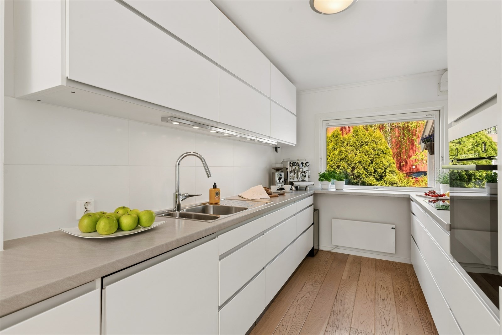 Velutstyrt kjøkkeninnredning fra IKEA (2011) med integrerte hvitevarer og lys under overskap, flislagte veggflater og god benkplass. Galleribilde