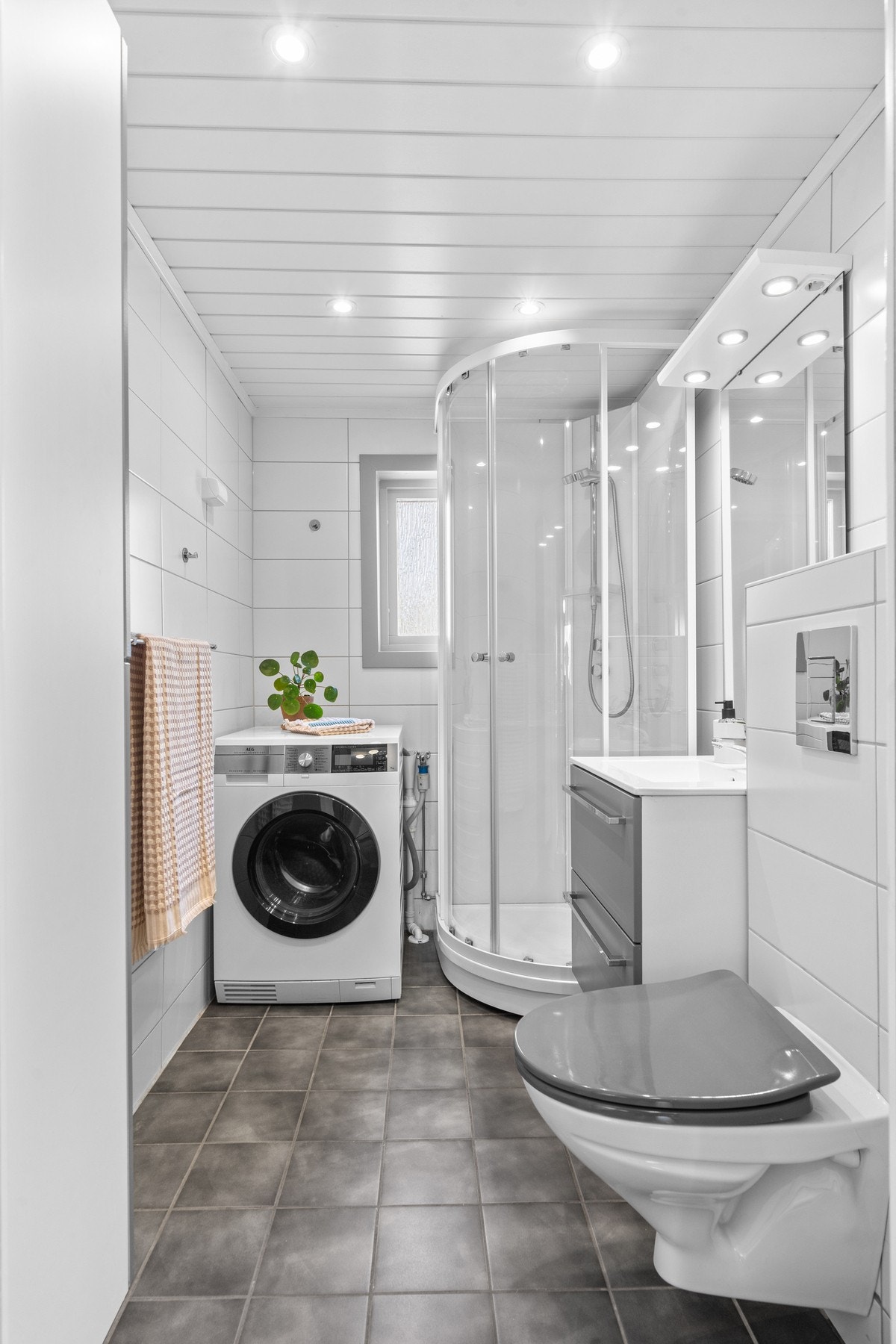Pent, flislagt bad fra 2013 med varmekabler i gulv. Badet er innredet med servantskap, veggmontert toalett, dusjkabinett med skyvedører, opplegg for vaskemaskin og praktisk oppbevaring i hyller. Galleribilde