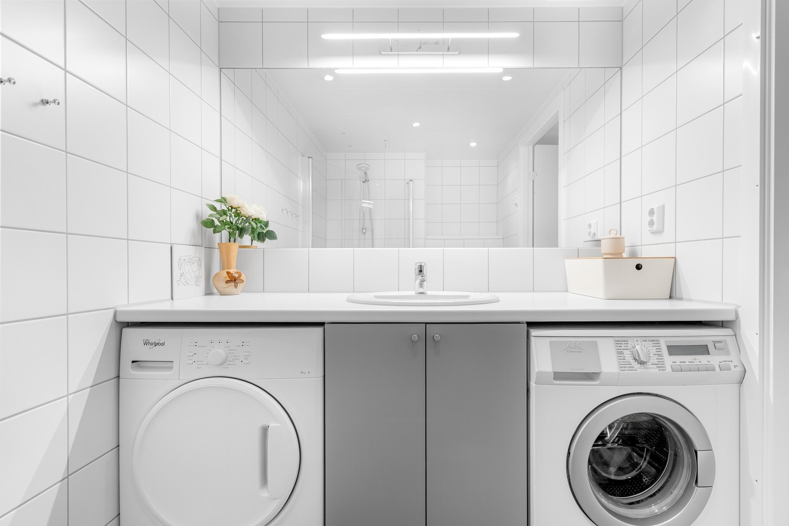 Tidløs baderomsinnredning med heldekkende benkeplate med nedfelt servant og stort speil med belysning over. Praktisk med plass og opplegg for både vaskemaskin og tørketrommel under benkeplaten. Galleribilde